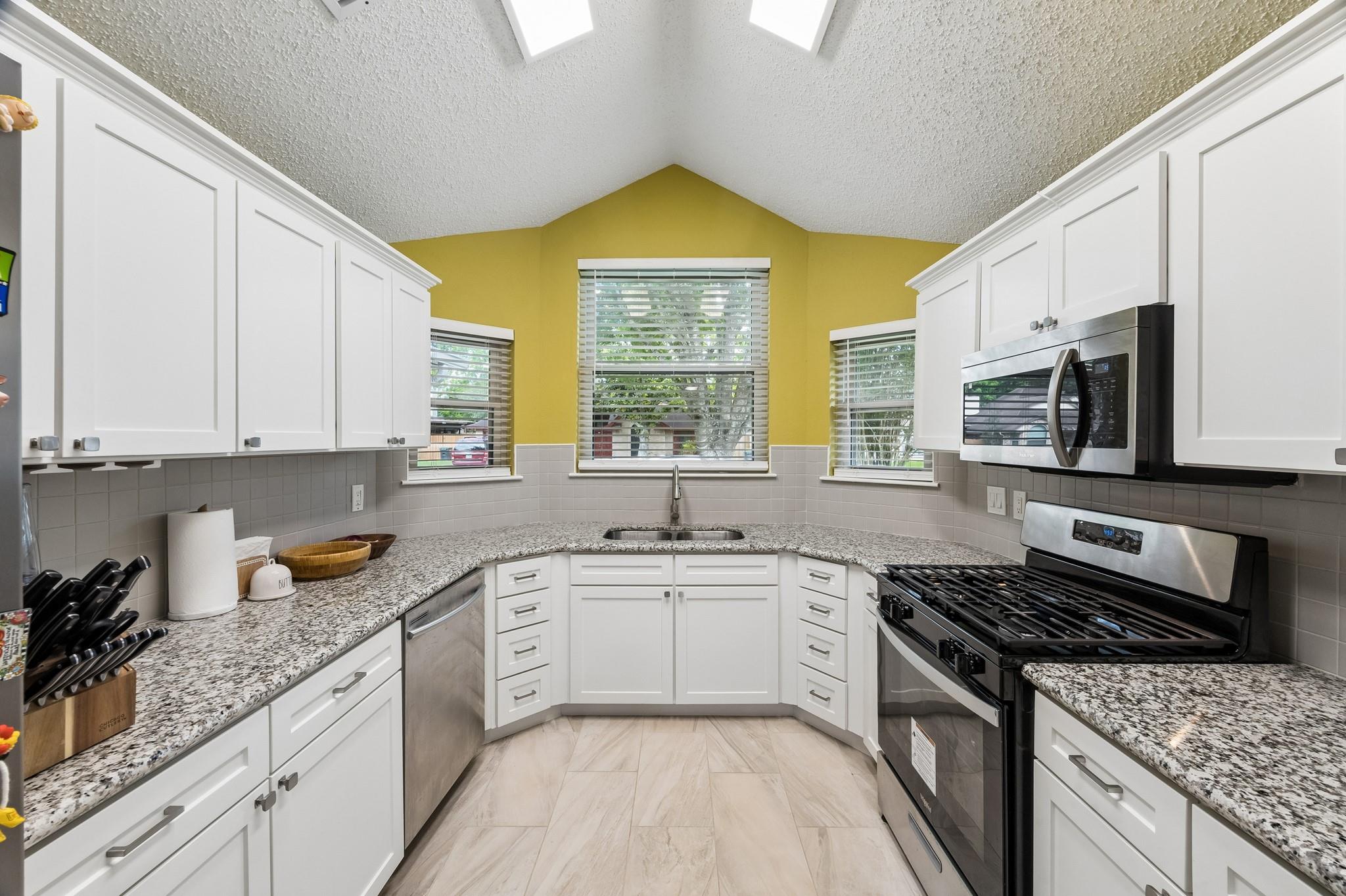 Kitchen with white cabinets, granite counters, stainless steel appliances, and a yellow accent wall.