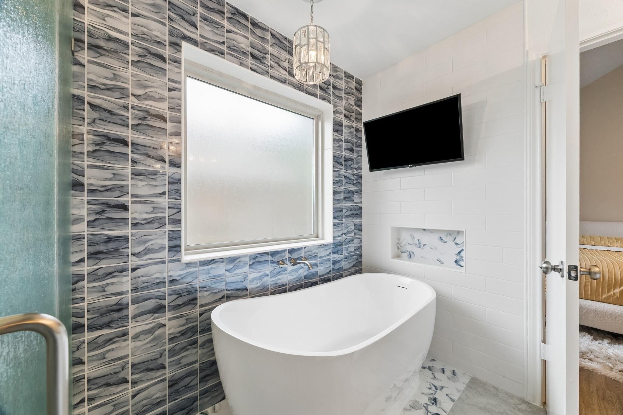 Modern bathroom with a freestanding tub and blue-gray patterned tile around a frosted window.