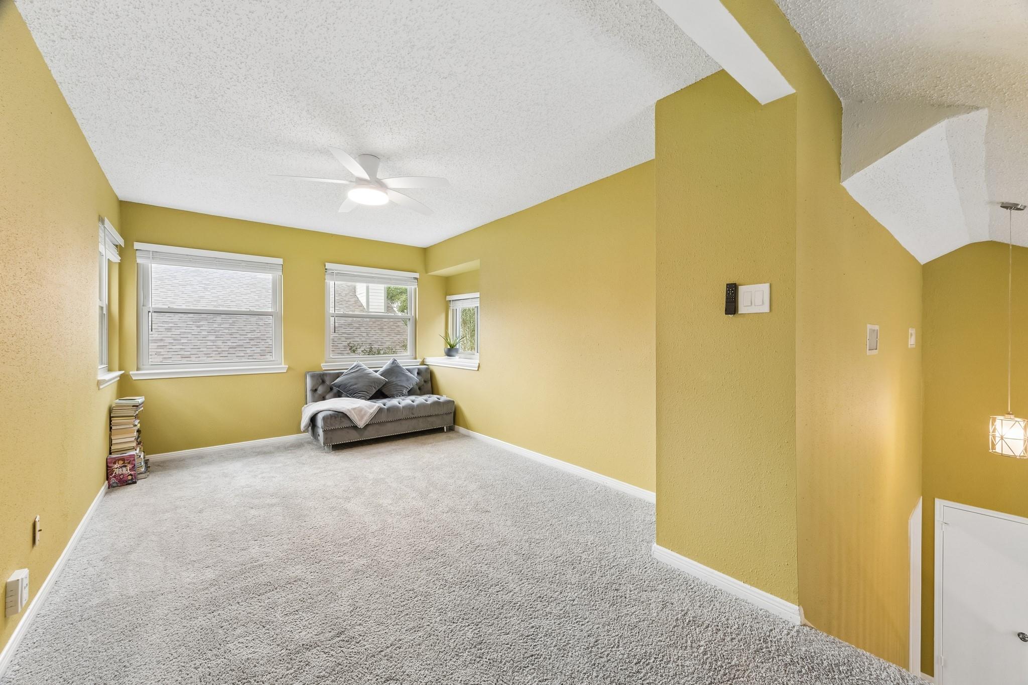 Upstairs sitting area with mustard-yellow walls, gray carpet, and a tufted loveseat by the windows.