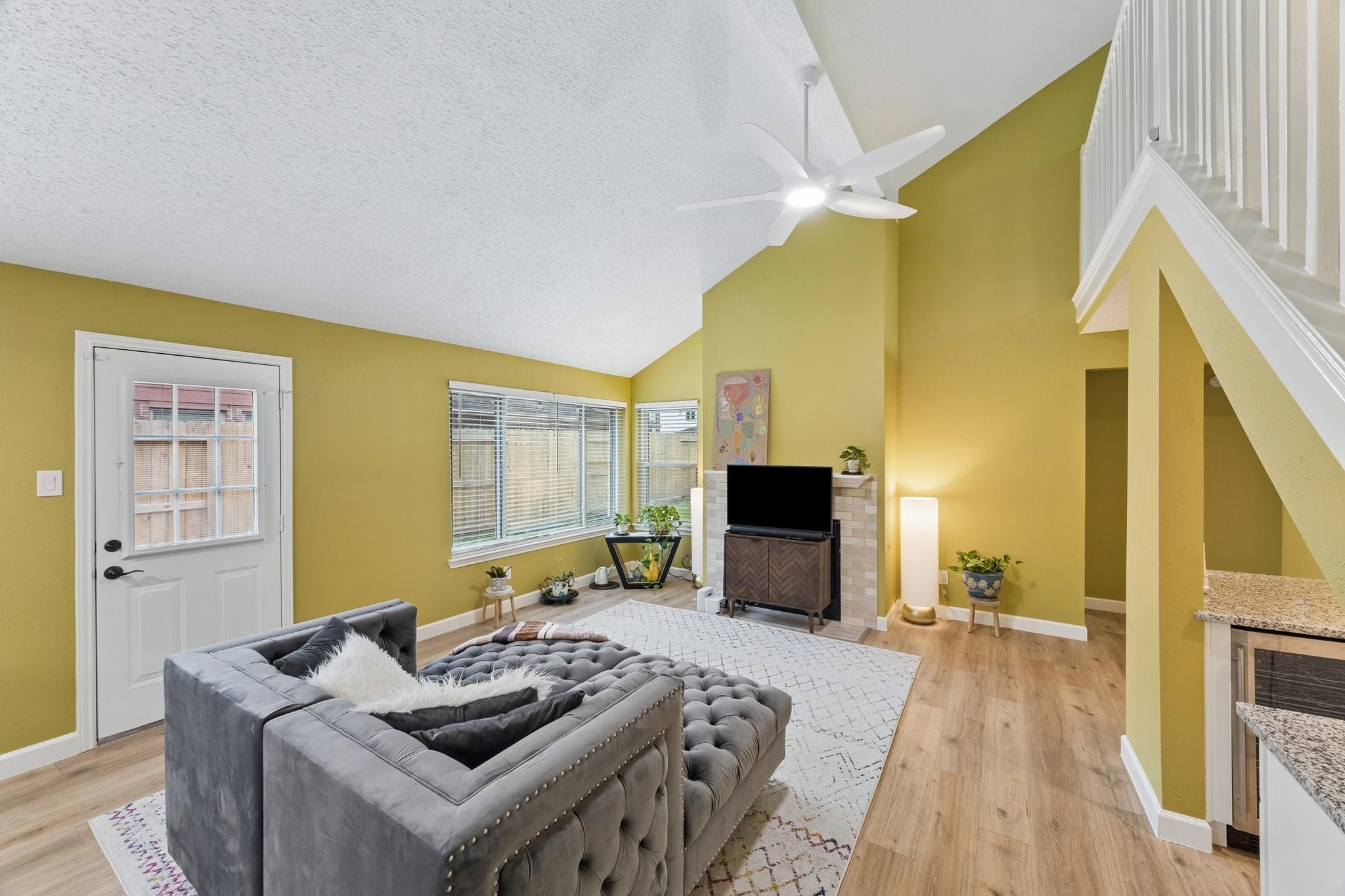 Living room with a gray tufted sectional, mustard-yellow walls, large windows, and an open staircase.