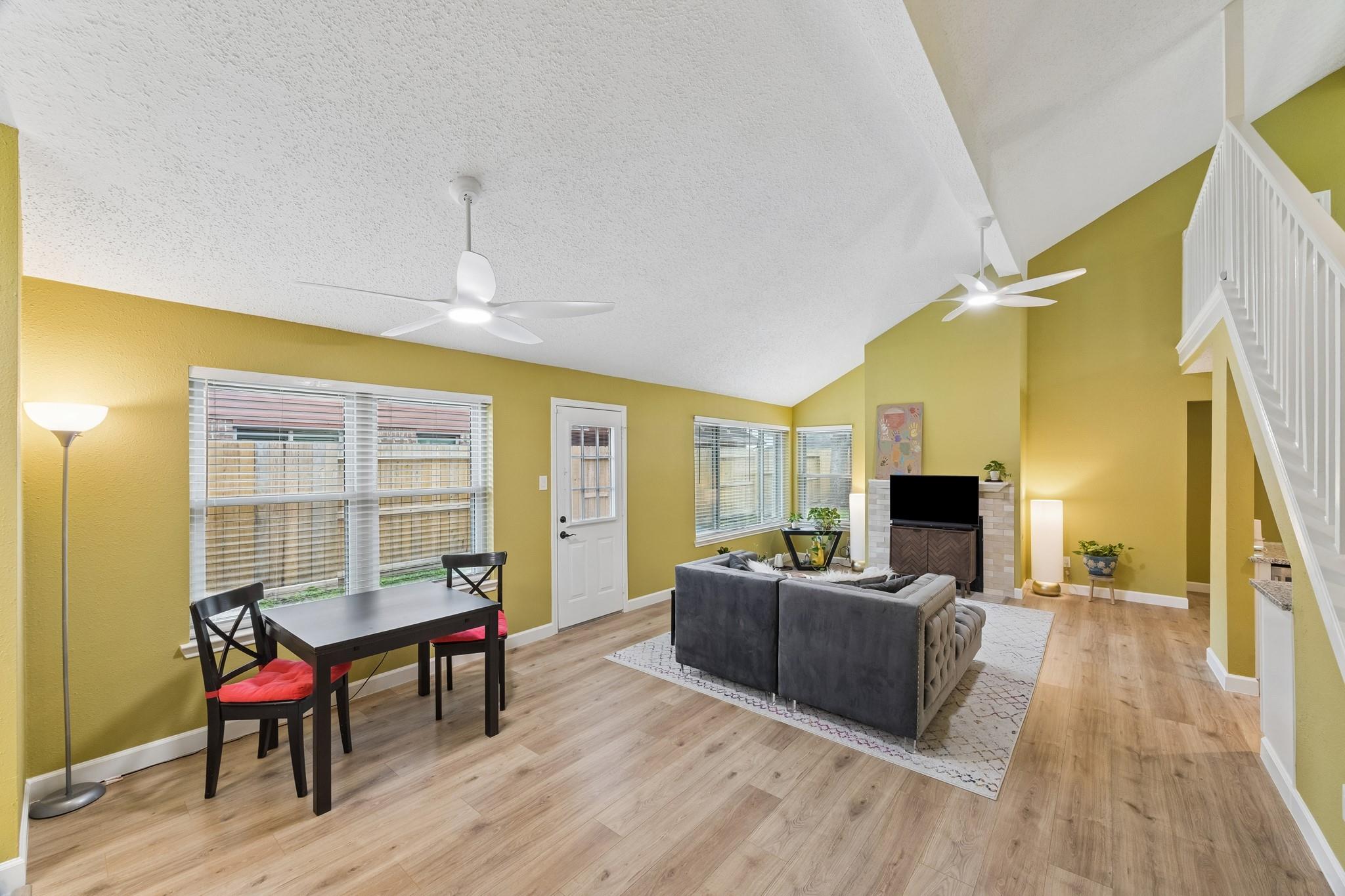 Open-plan living and dining room with mustard walls, gray sectional, fireplace, and staircase.