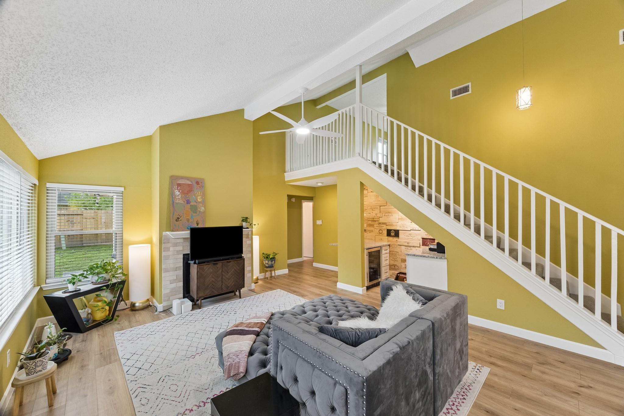 Living room with a gray sectional, vaulted ceiling, and white staircase leading to an open loft.