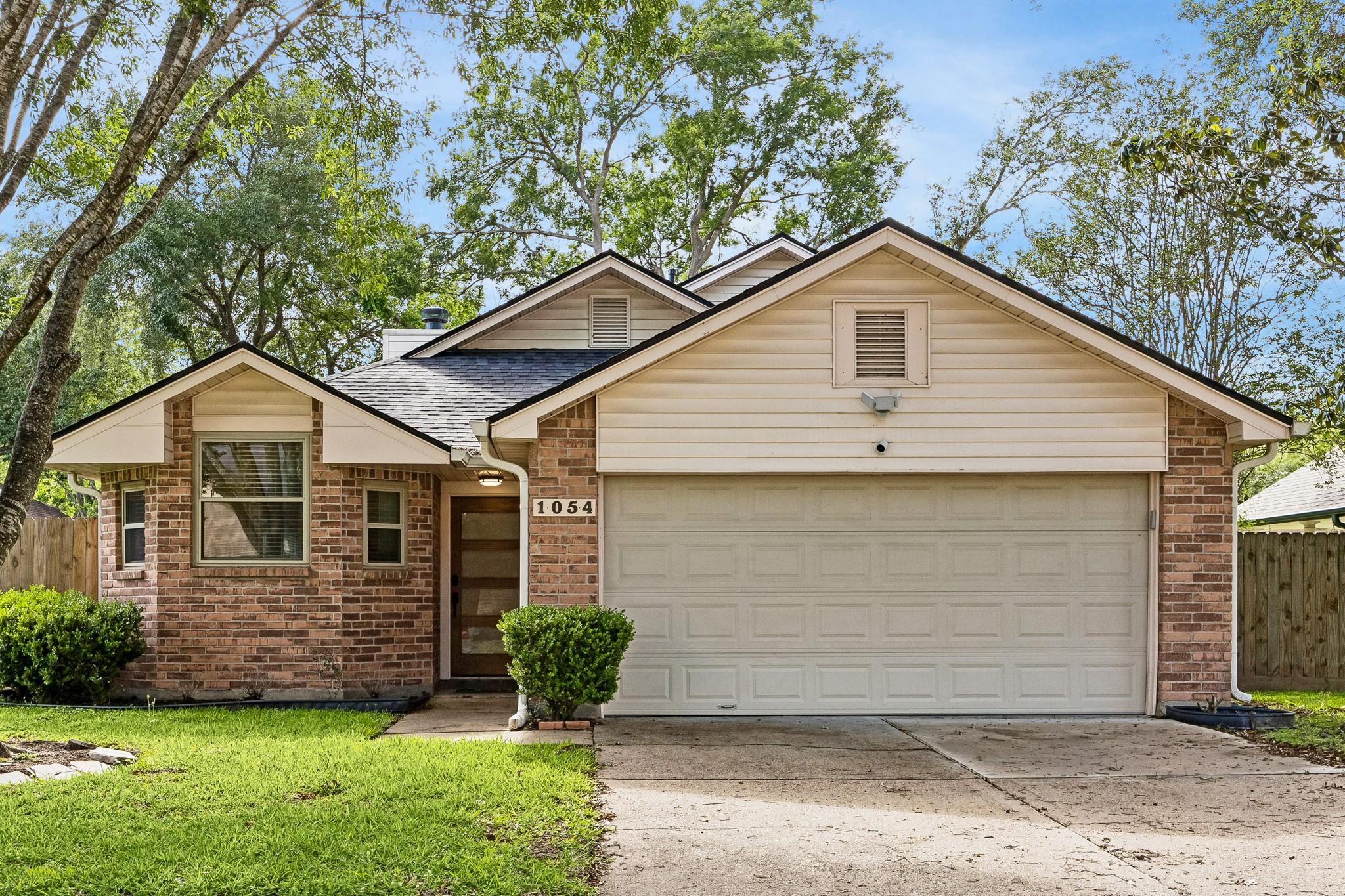Single-story brick house with beige siding, a two-car garage, and house number 1054.