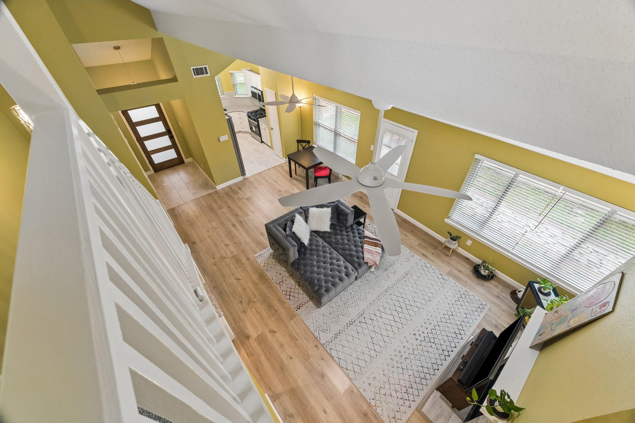 Furnished living room viewed from above, with vaulted ceiling, gray sofa, and open kitchen beyond.
