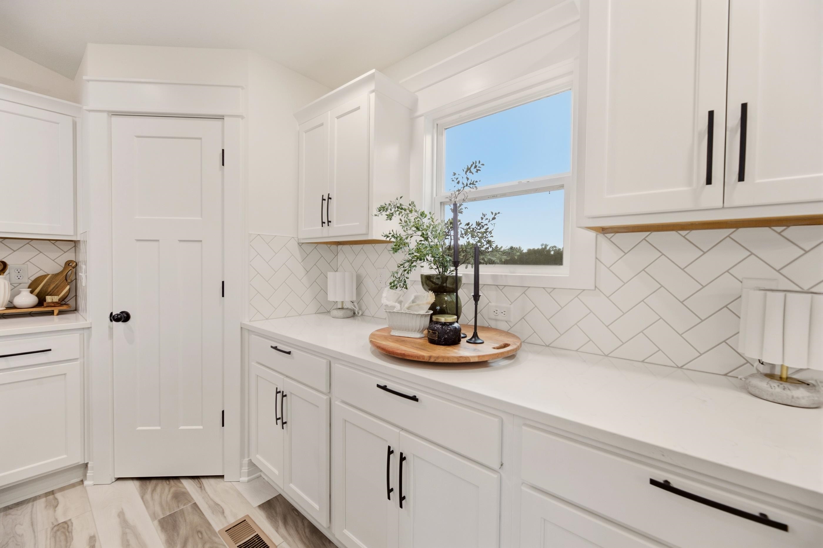 White kitchen with black cabinet hardware, geometric tile backsplash, and a window over the countertop.
