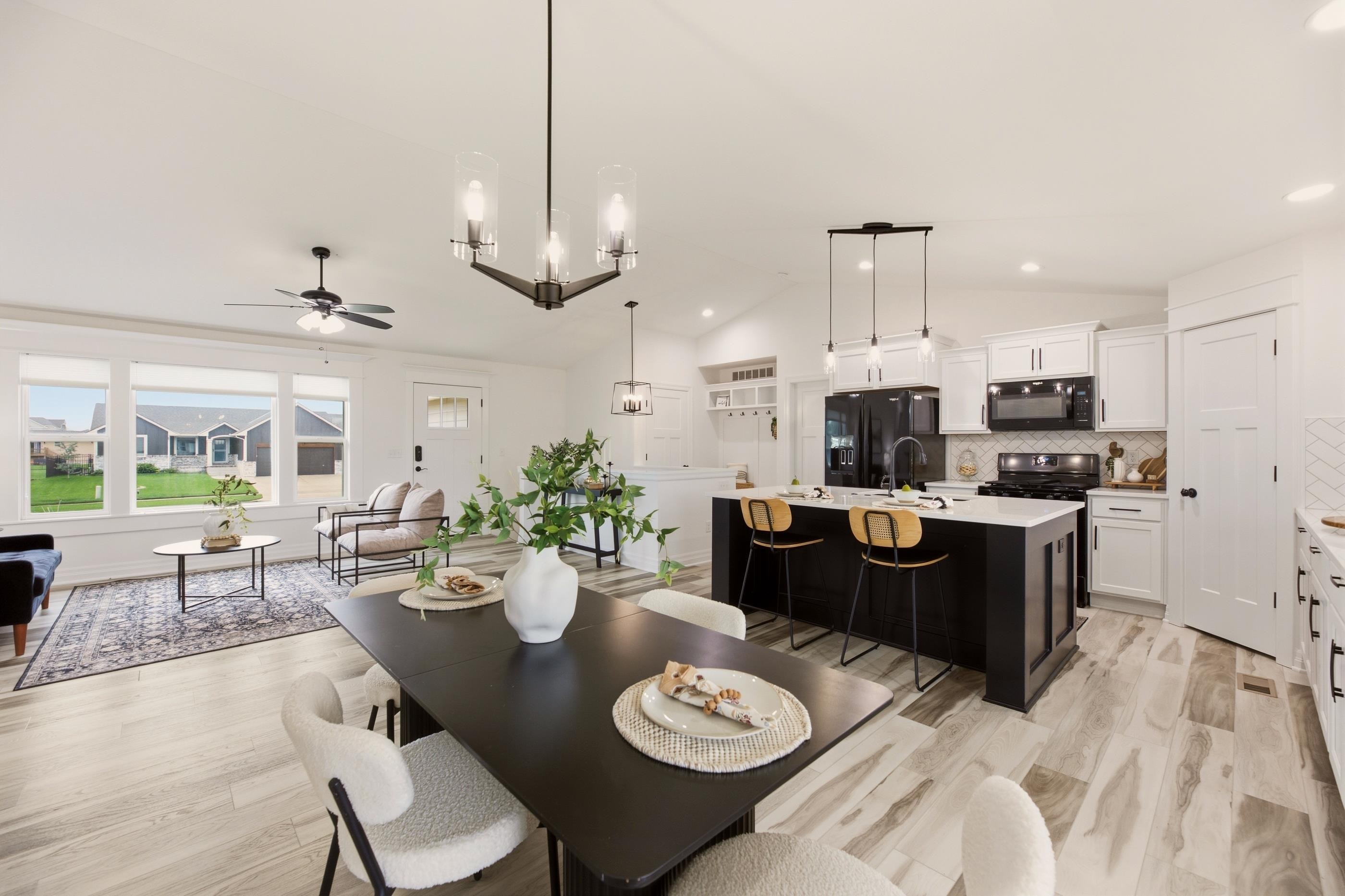 Open-plan kitchen and living room with a black island, white cabinetry, and large windows.
