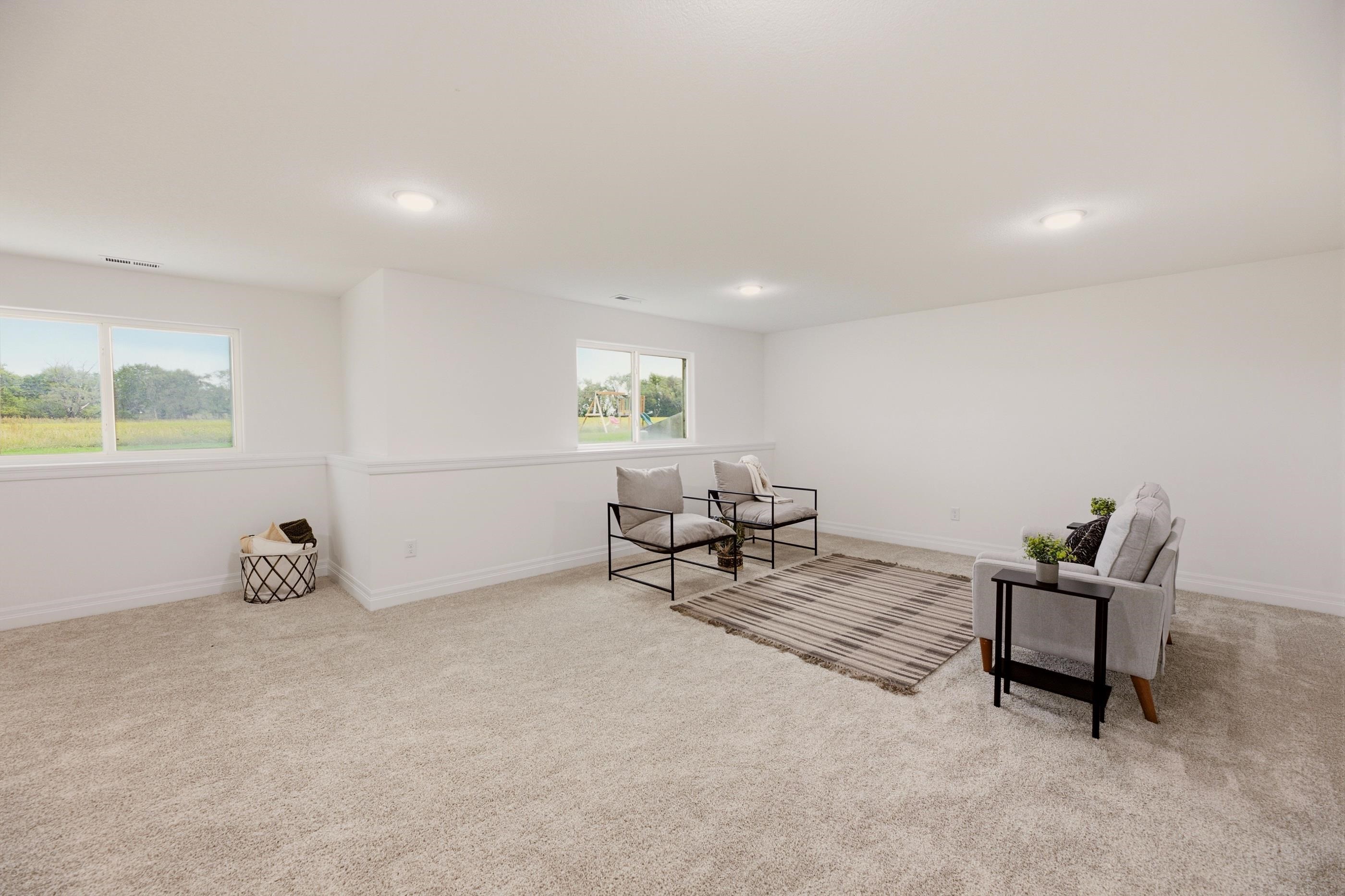 Staged sitting room with beige carpet, black-framed chairs, and windows overlooking greenery.