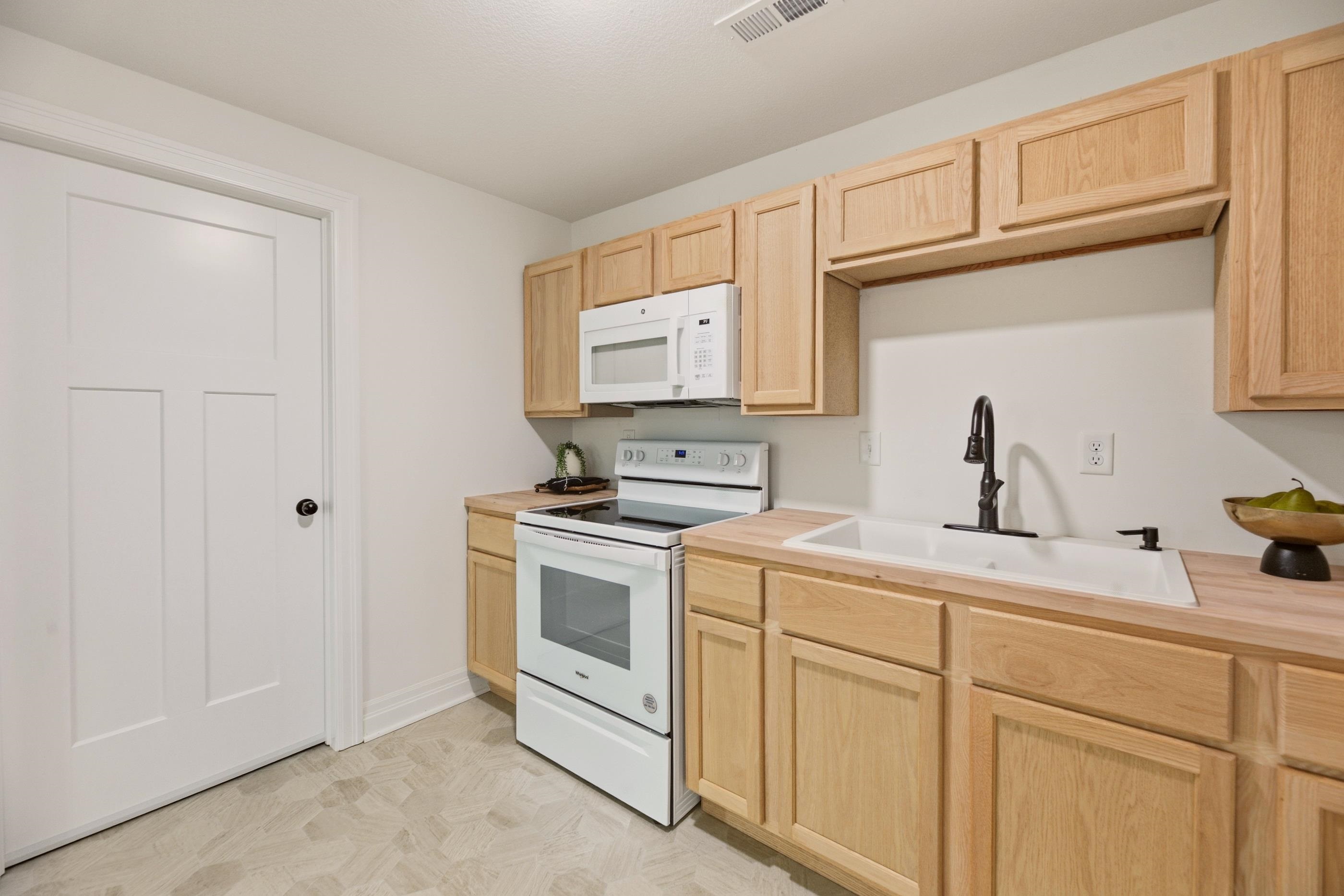 Kitchen with light wood cabinets, white appliances, and a sink with a dark faucet.