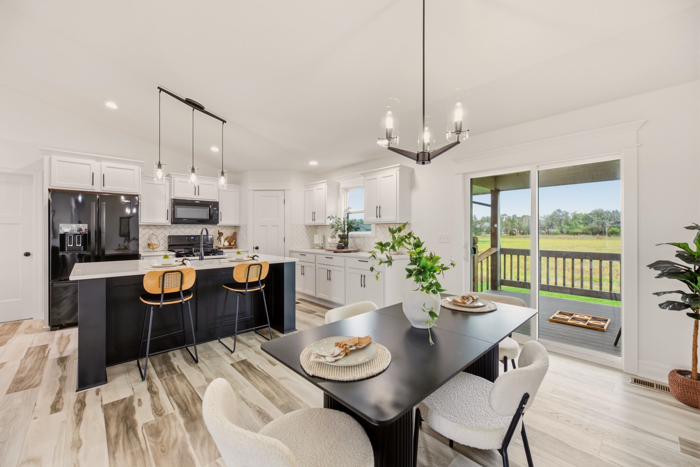 Open-plan kitchen and dining area with white cabinets, black island, and sliding doors to a covered deck.