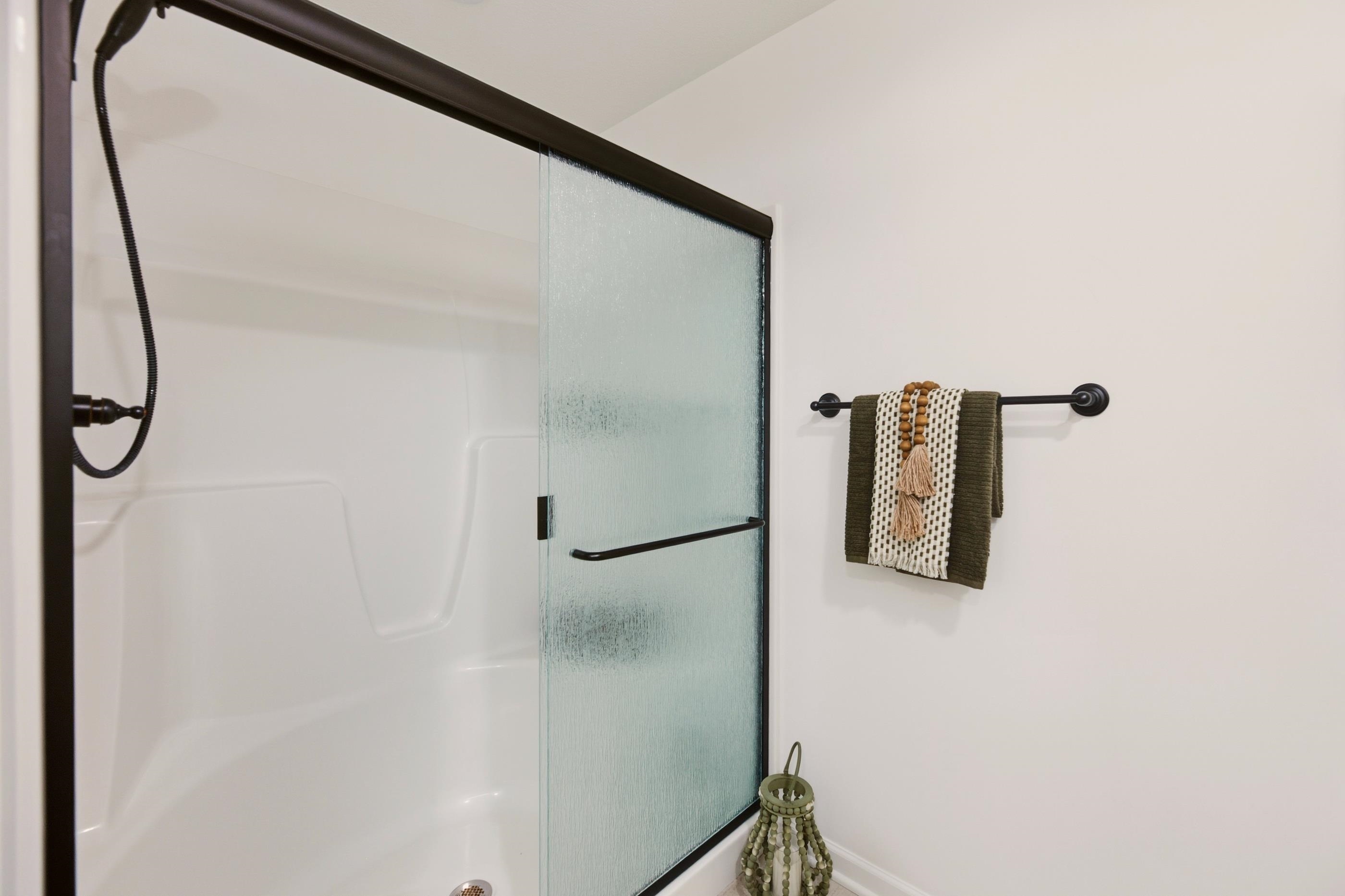 Bathroom shower with textured glass door, white enclosure, and black fixtures beside neatly hung towels.