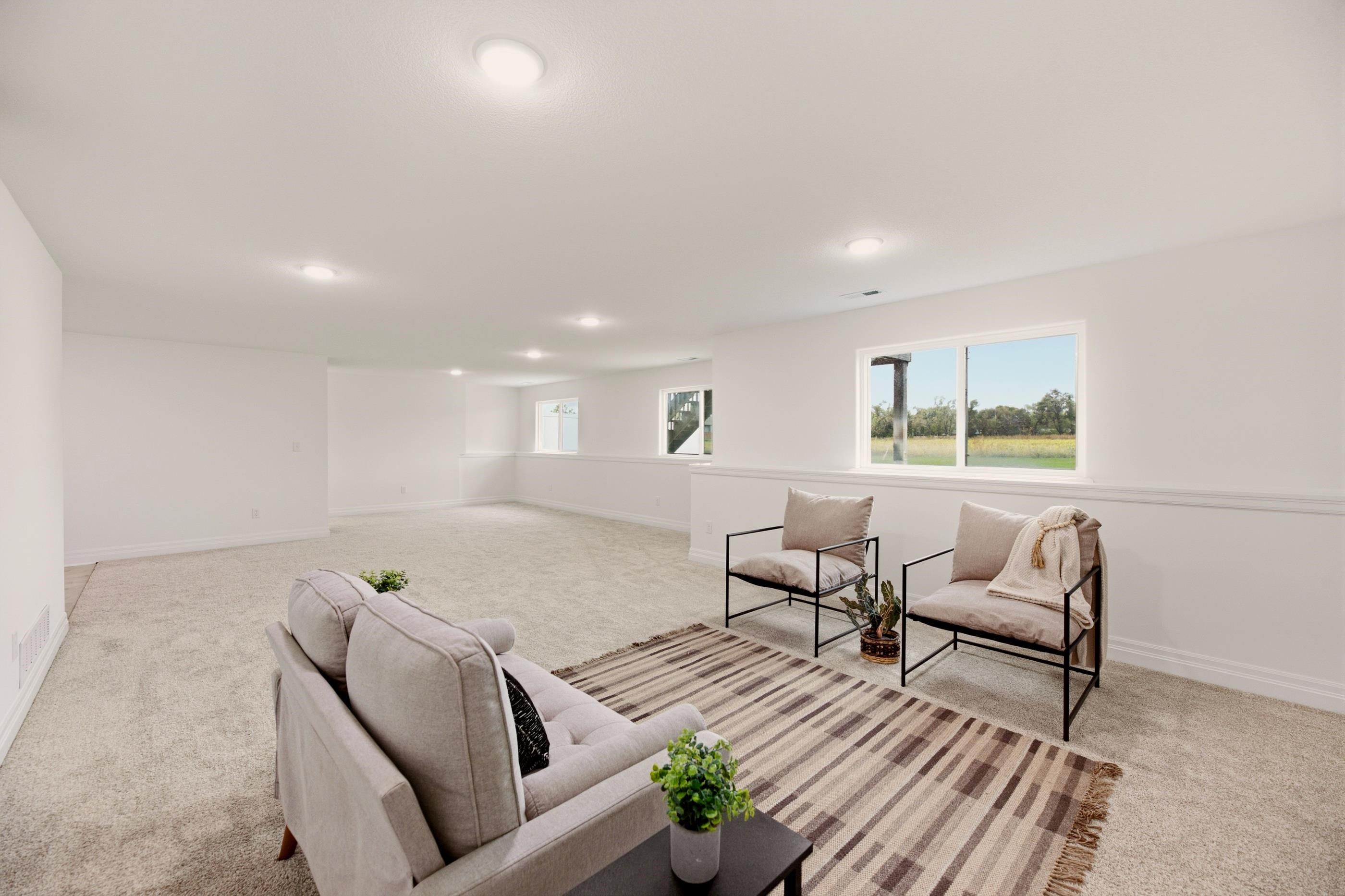 Staged basement living room with a sofa, two armchairs, striped rug, and windows overlooking the yard.