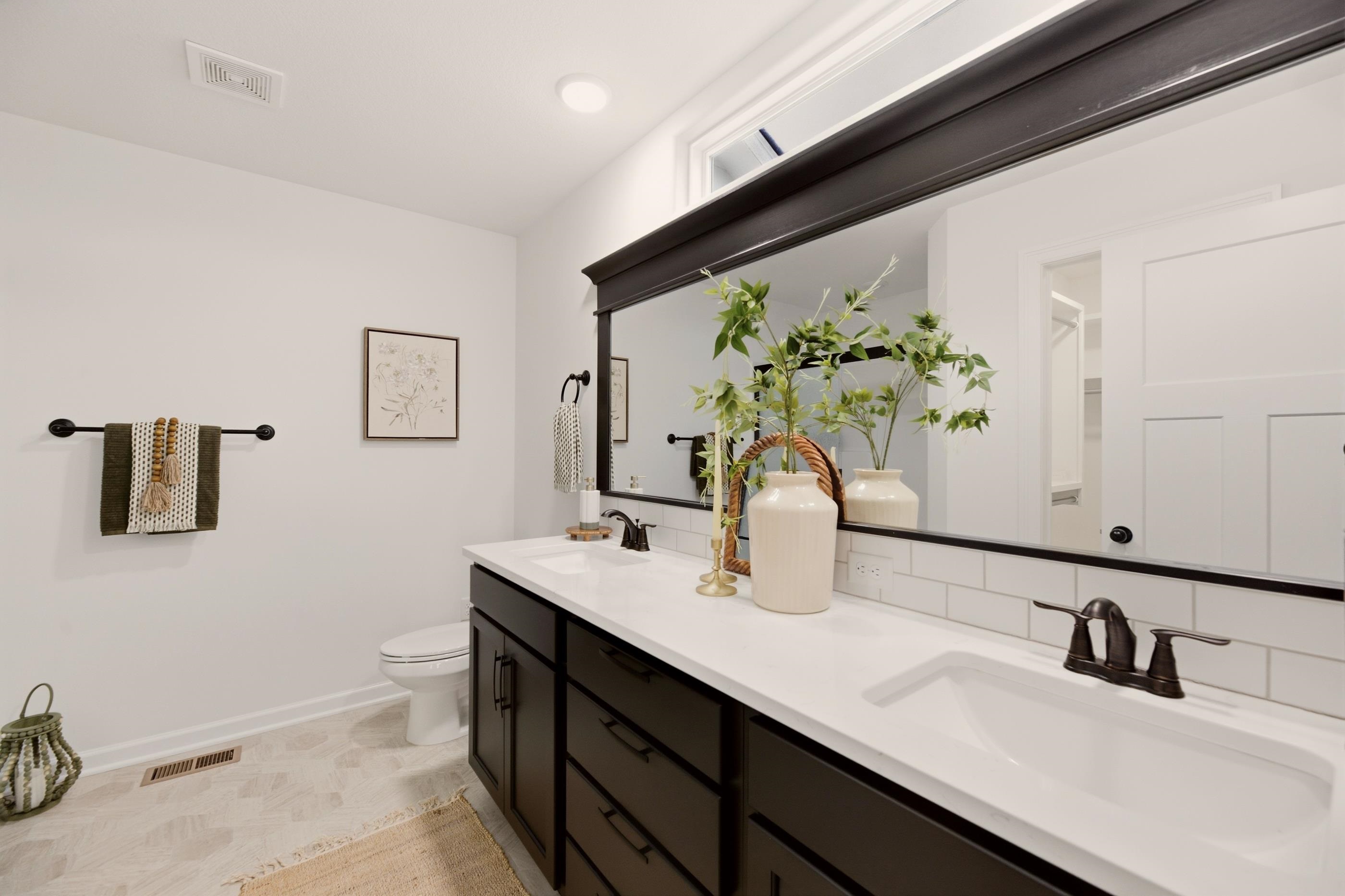 Bright bathroom with a white double-sink vanity, dark cabinetry, and large framed mirror.