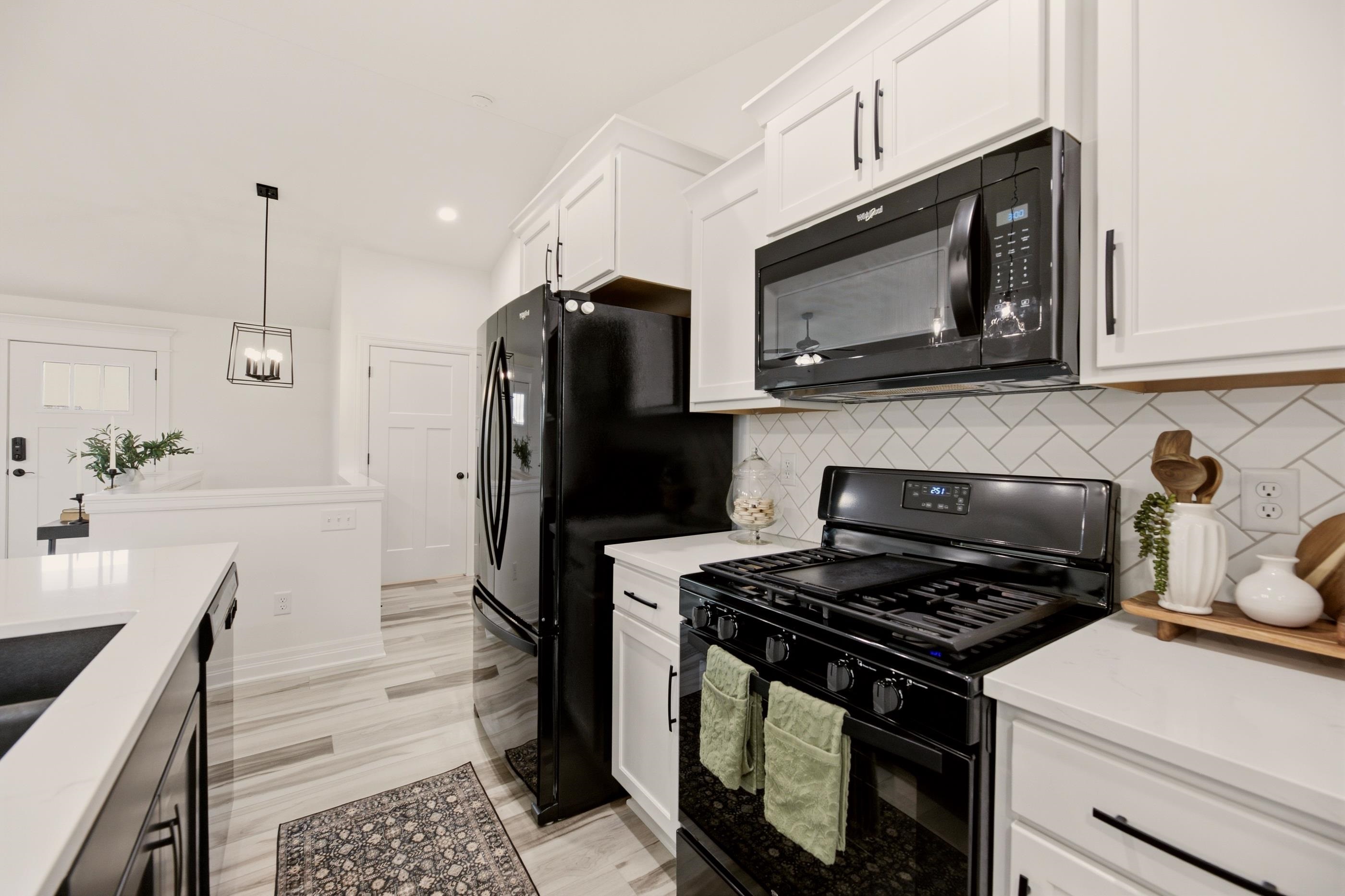 Bright kitchen with white cabinets, diagonal tile backsplash, and black appliances.
