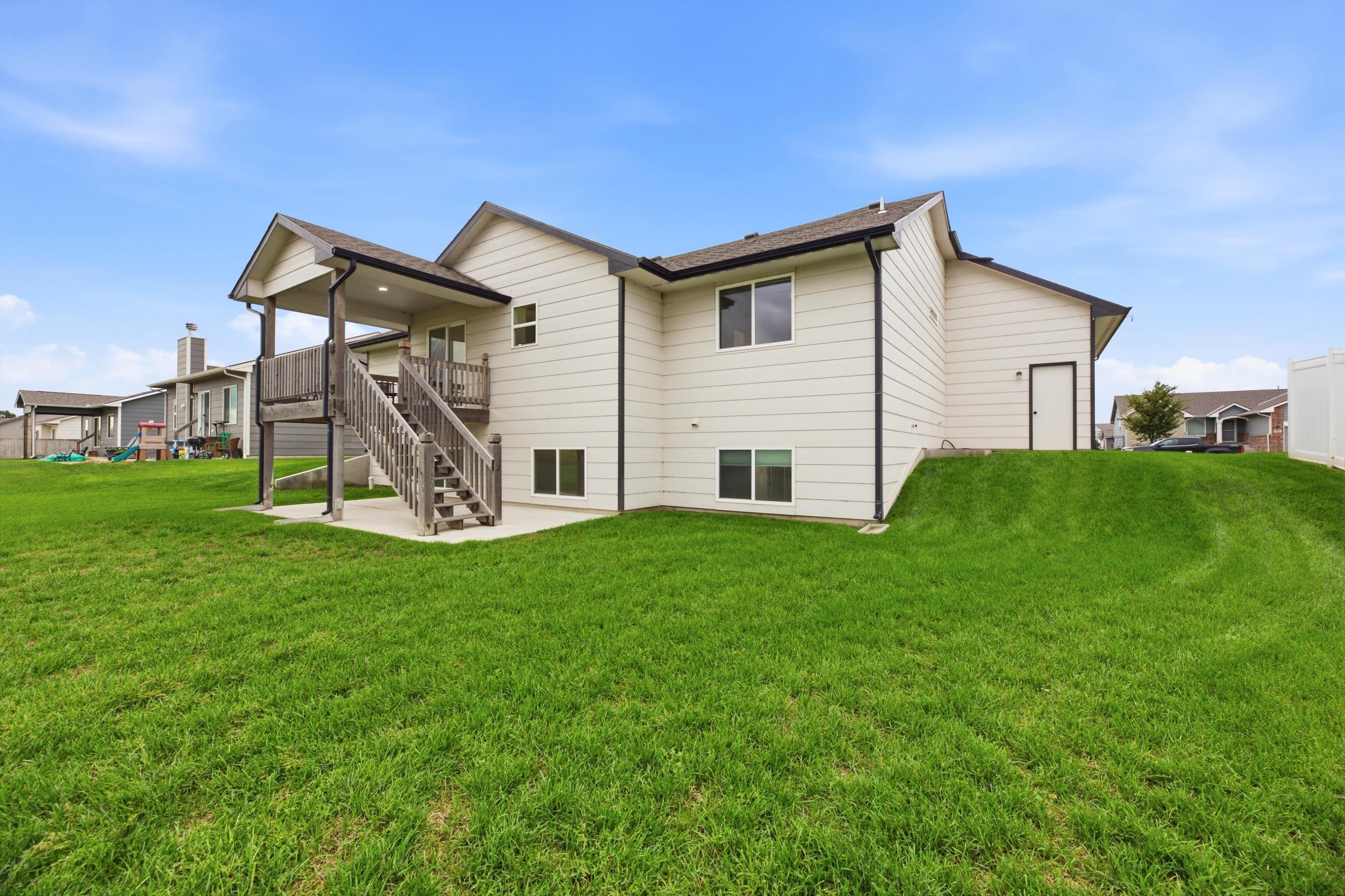 Rear of a light-sided home with a raised deck and stairs overlooking a broad green lawn.
