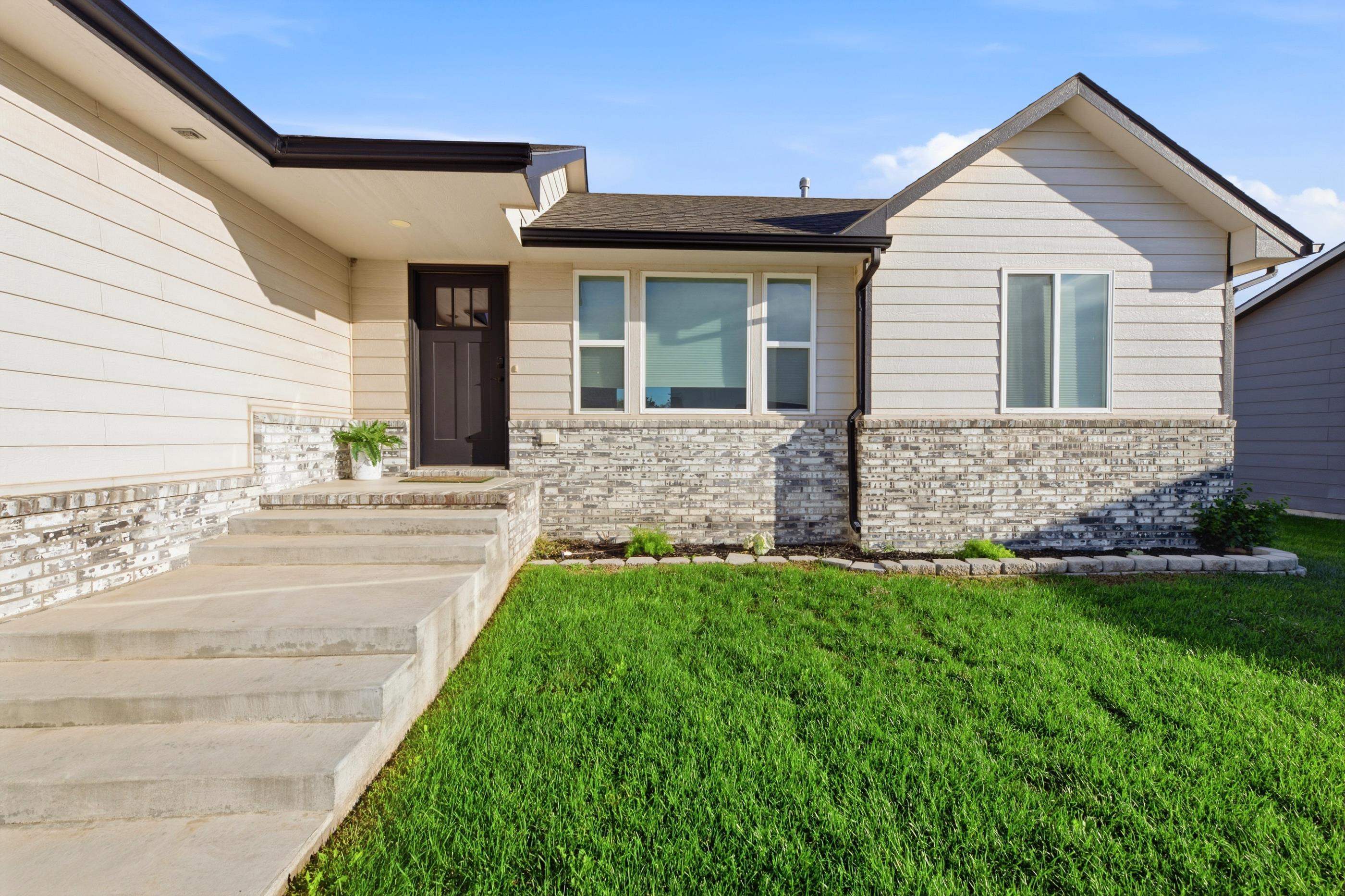 Home exterior with a covered entry, concrete steps, brick facade, and green lawn.