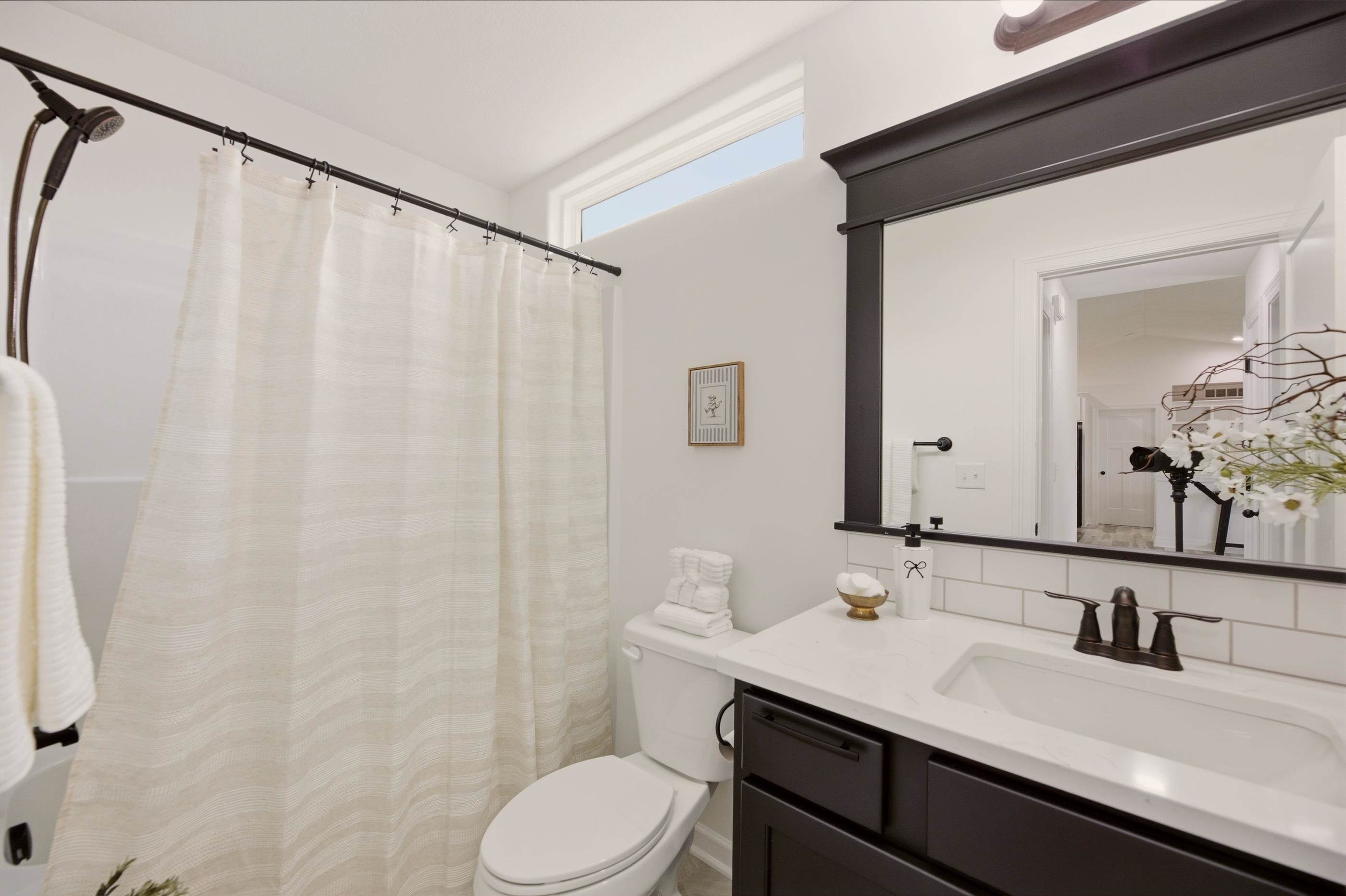 Bathroom with a white shower curtain, toilet, and dark vanity beneath a large mirror.