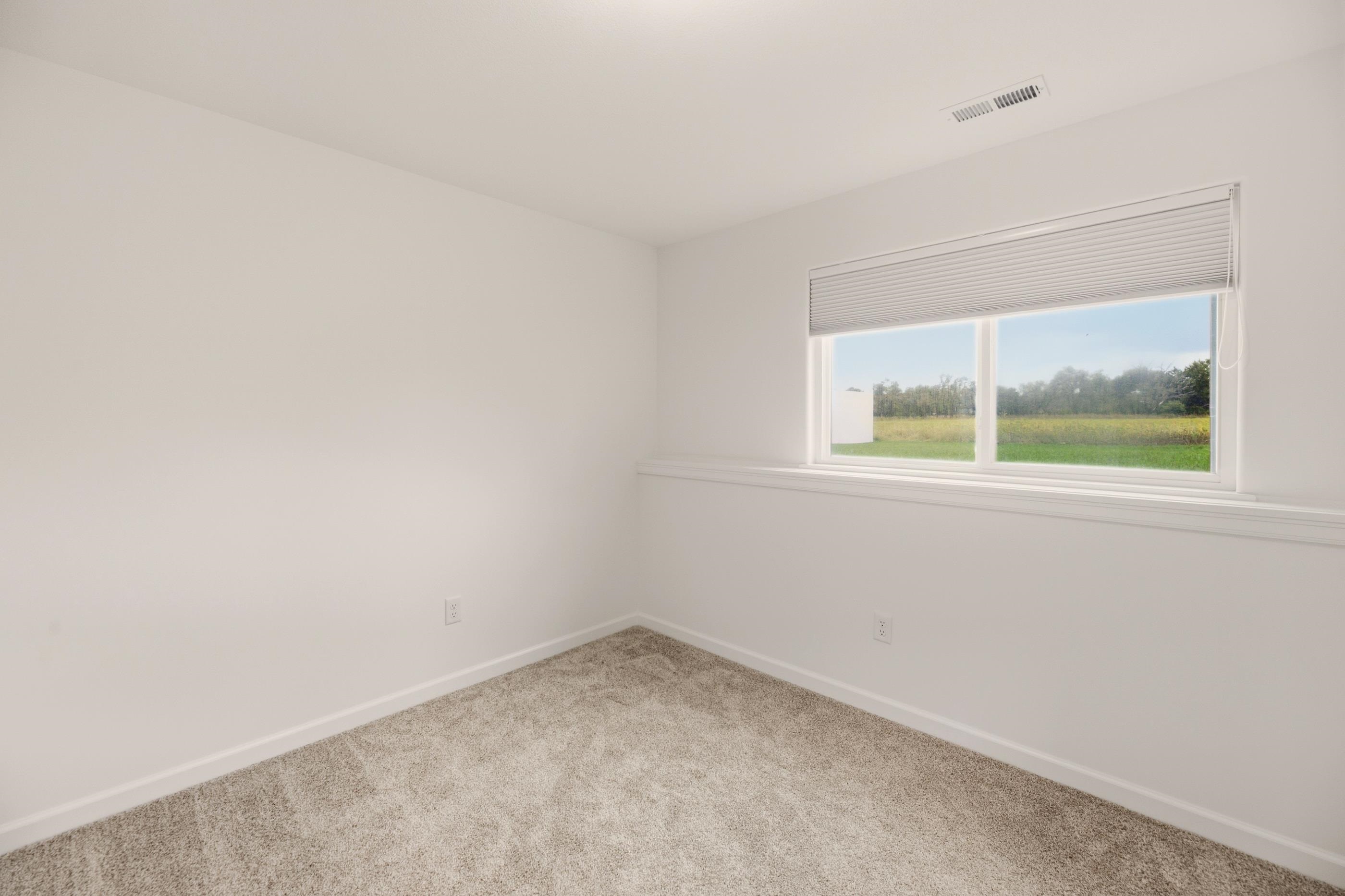 Empty carpeted room with white walls and a wide window overlooking a field.