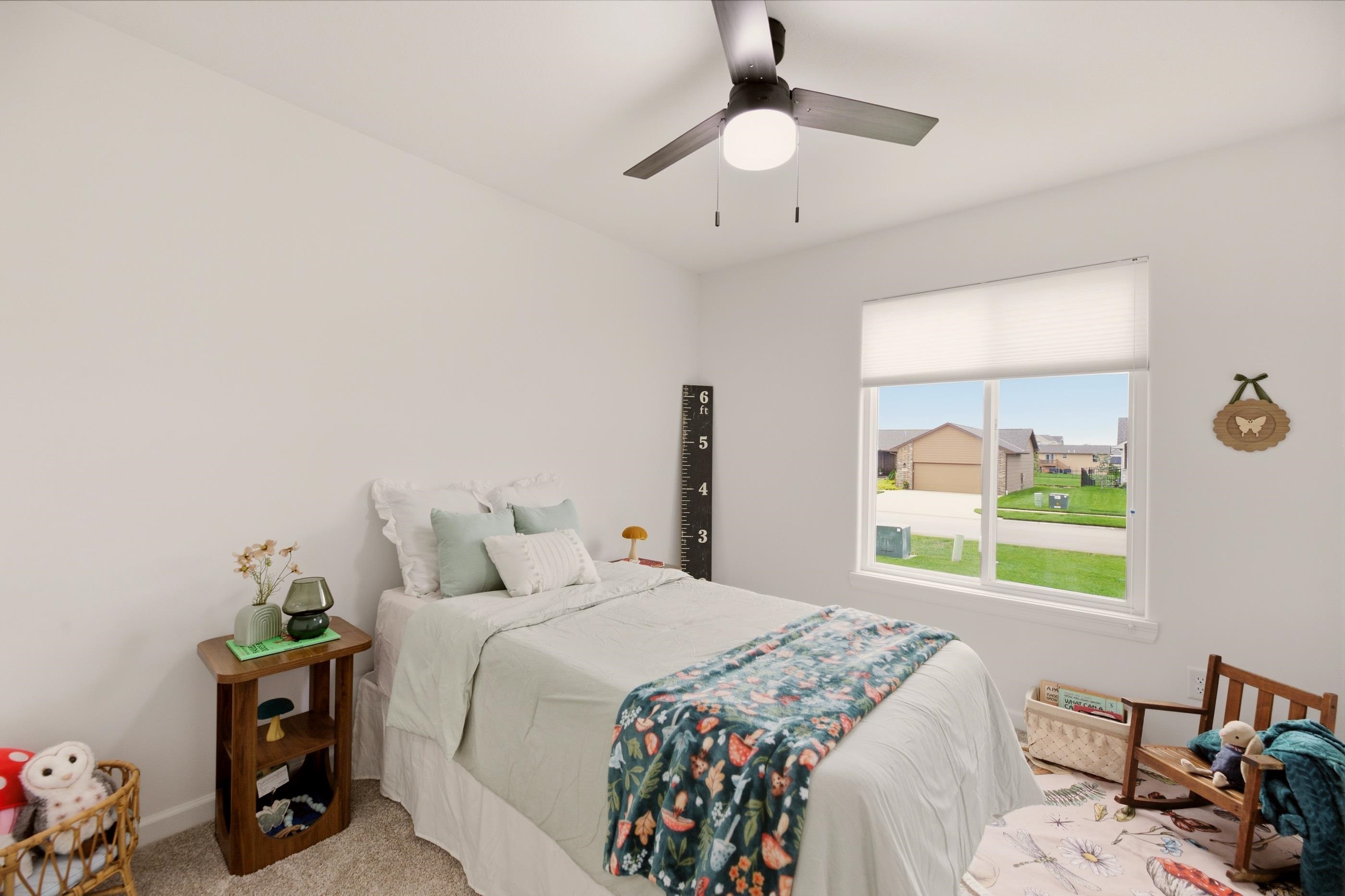 Bedroom with a white bed, floral blanket, and window overlooking neighboring homes.