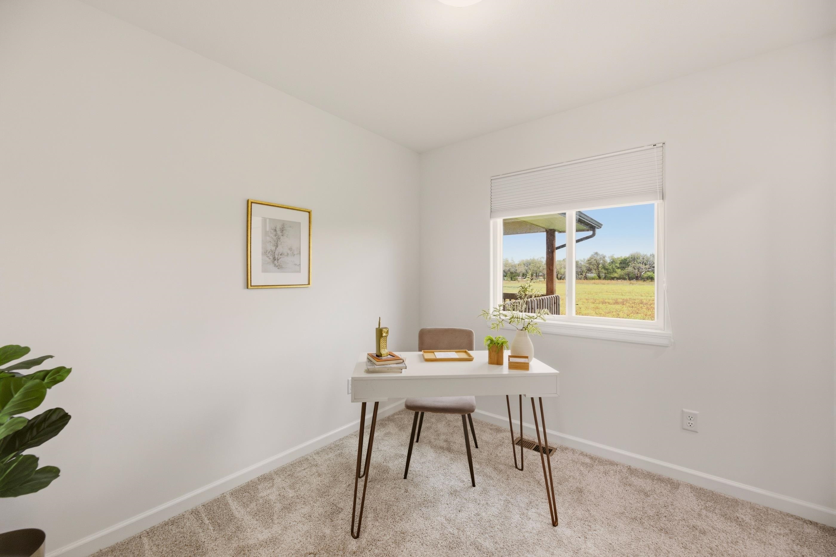 Staged home office with a white desk beside a window overlooking a grassy field.