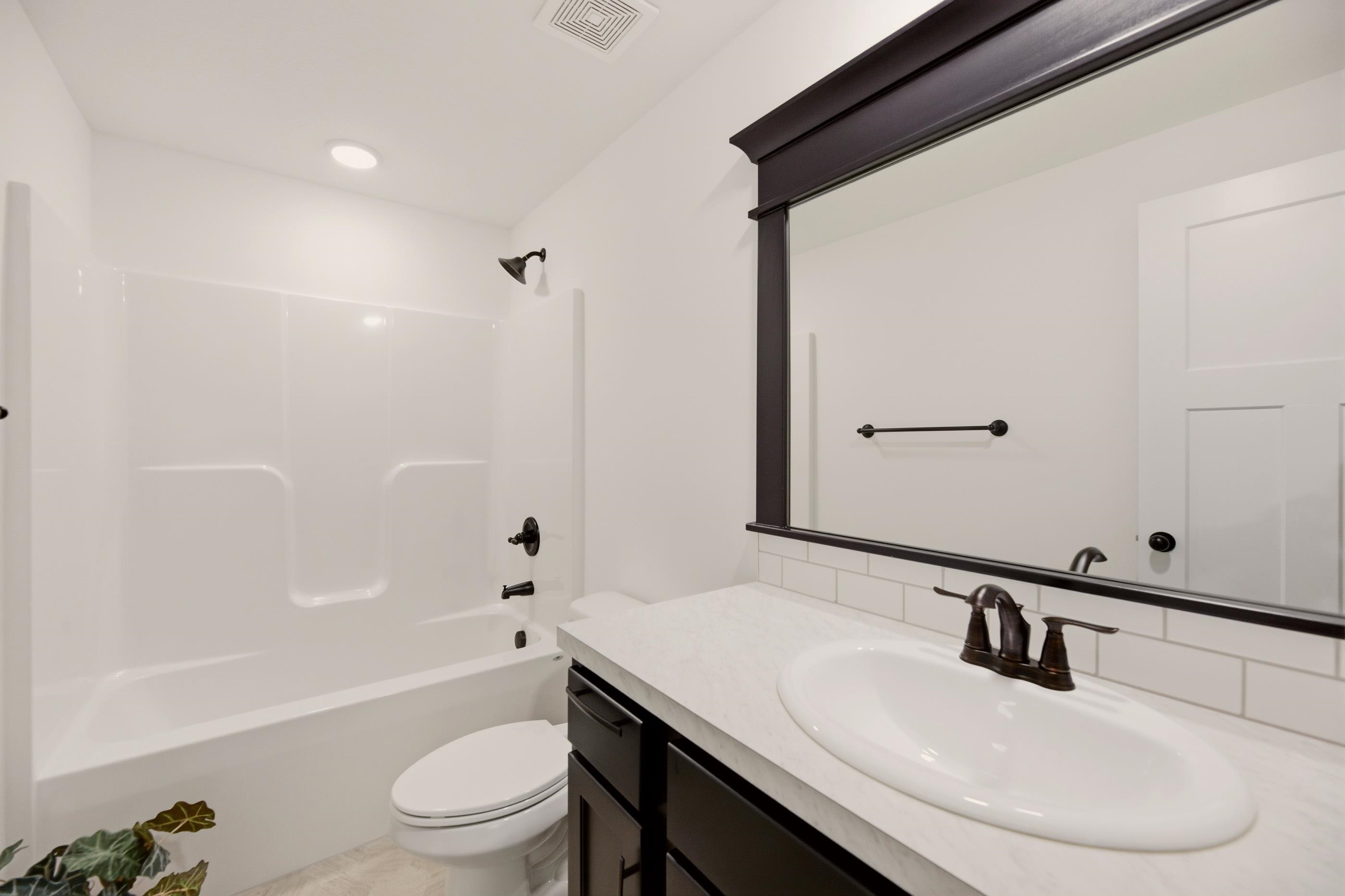 Bathroom with a tub and shower, dark vanity, white countertop, and large framed mirror.