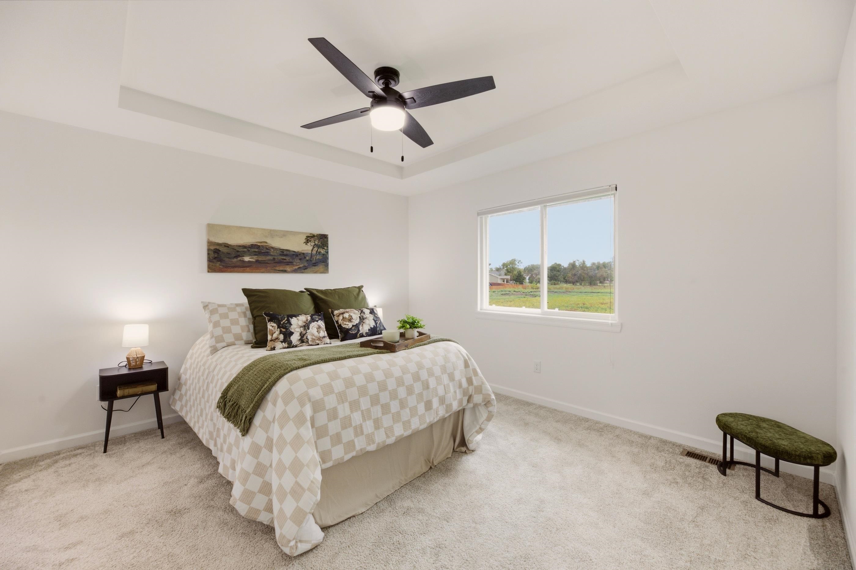 Staged bedroom with a checkered bedspread, olive accents, and a large window overlooking a grassy field.