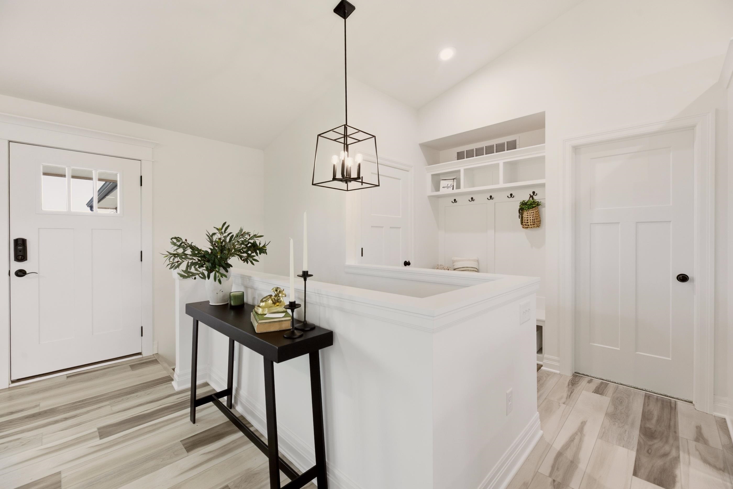 Bright entryway with built-in mudroom shelves, coat hooks, a white front door, and a black console table.