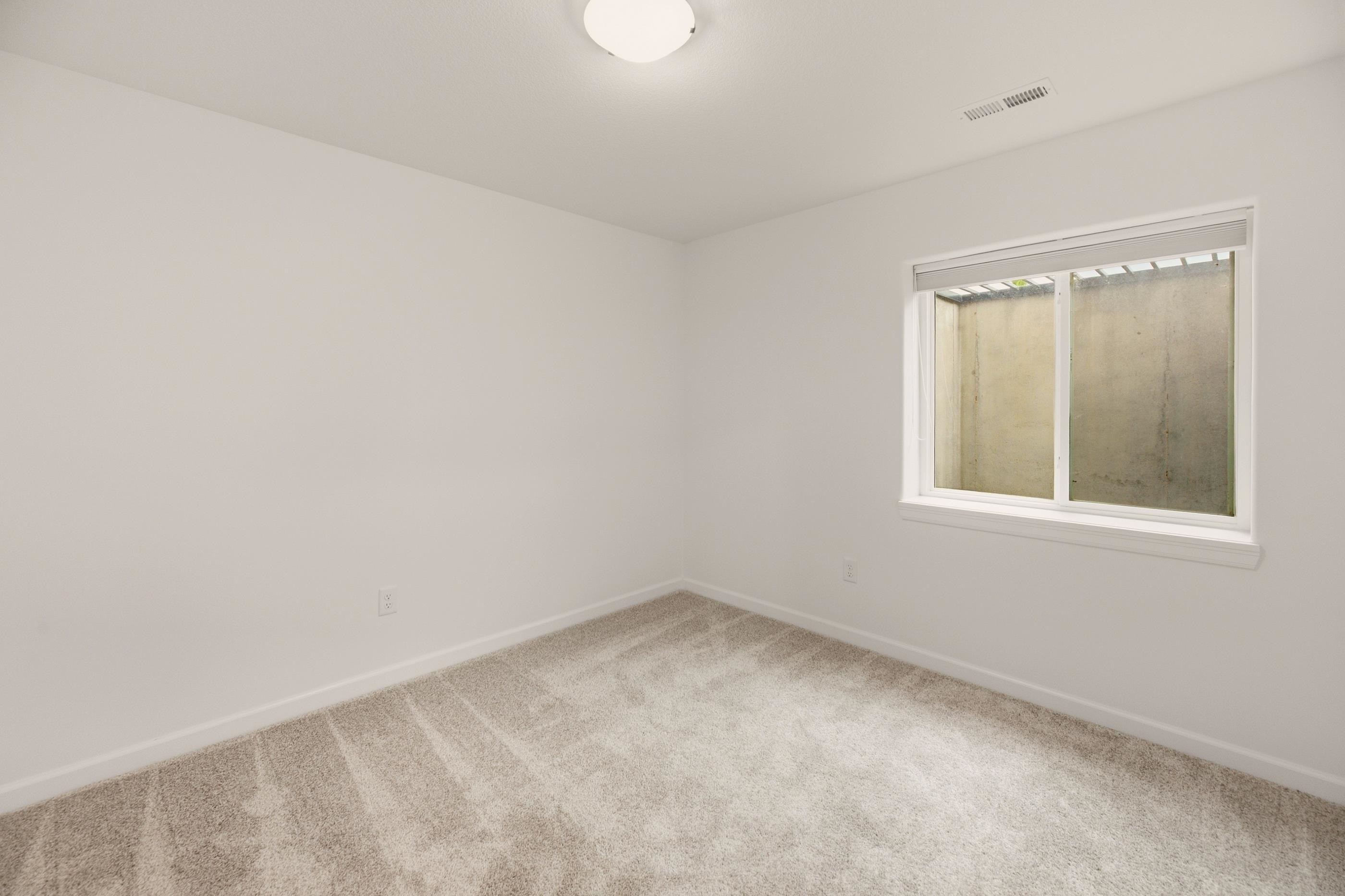 Empty carpeted room with white walls and a window with a raised blind.