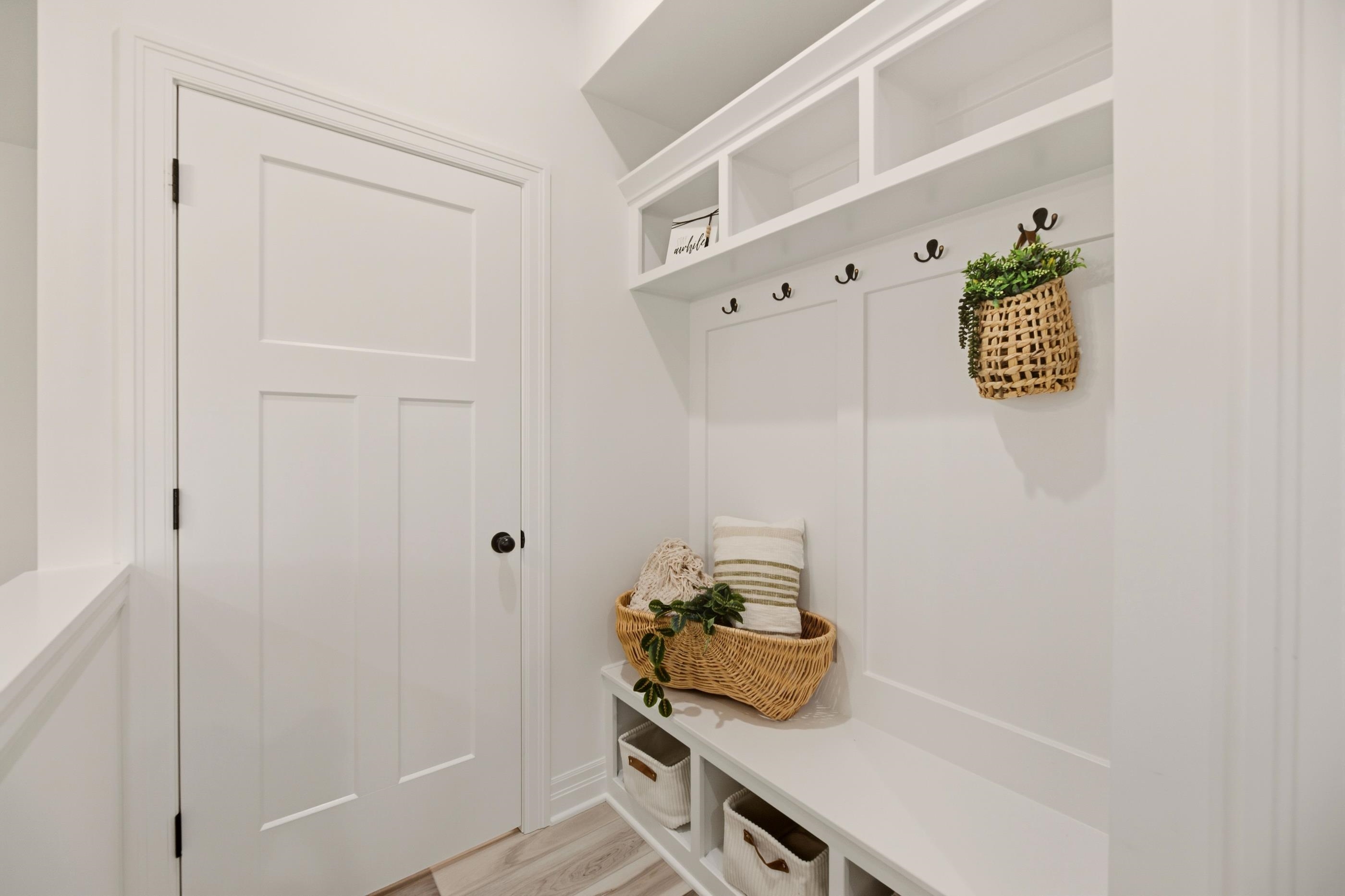 Staged white mudroom with built-in cubbies, black hooks, and a woven basket on the bench.
