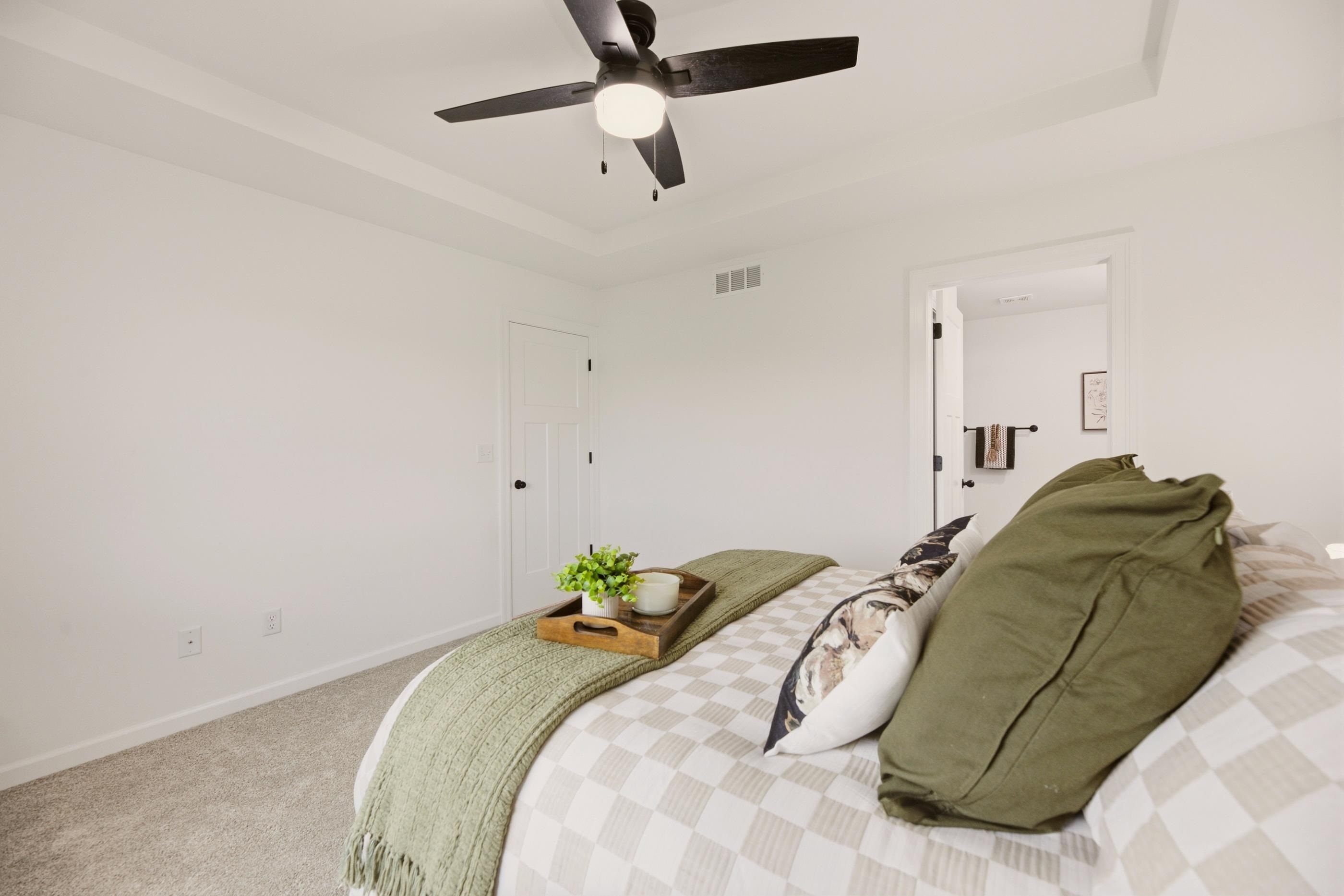 Staged bedroom with a checkered bed, green throw, and black ceiling fan.