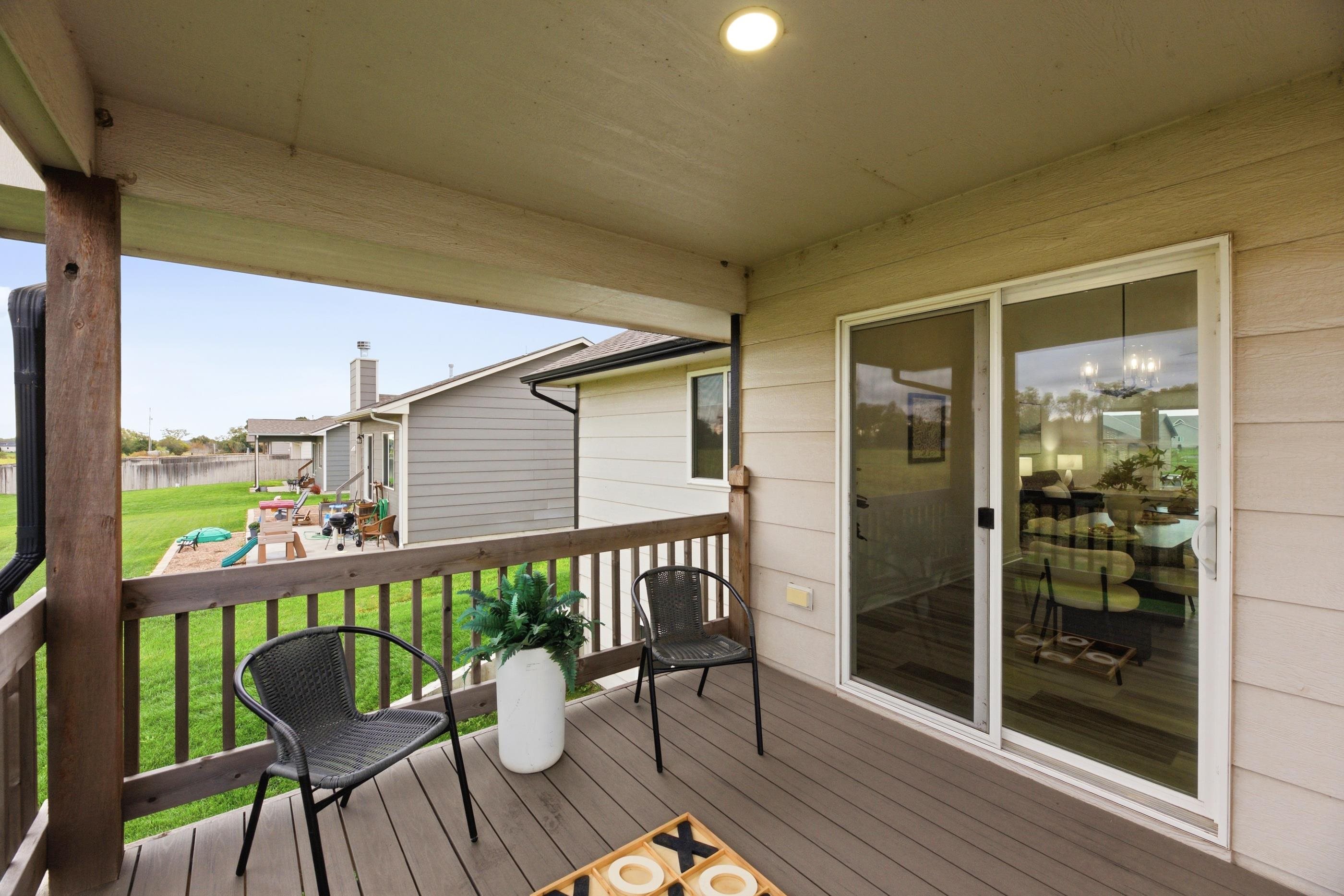 Covered wooden deck with black chairs and a potted plant overlooking a green backyard.