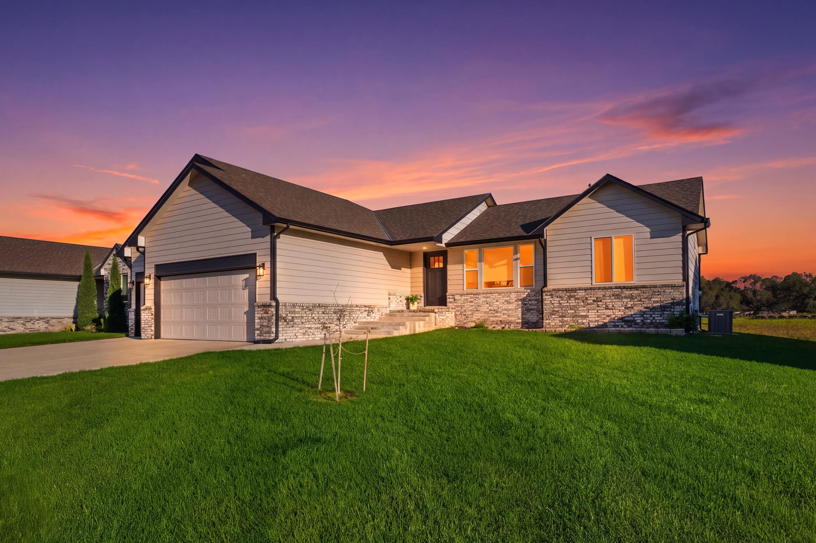 Modern single-story home with stone veneer, a two-car garage, and a broad lawn at sunset.