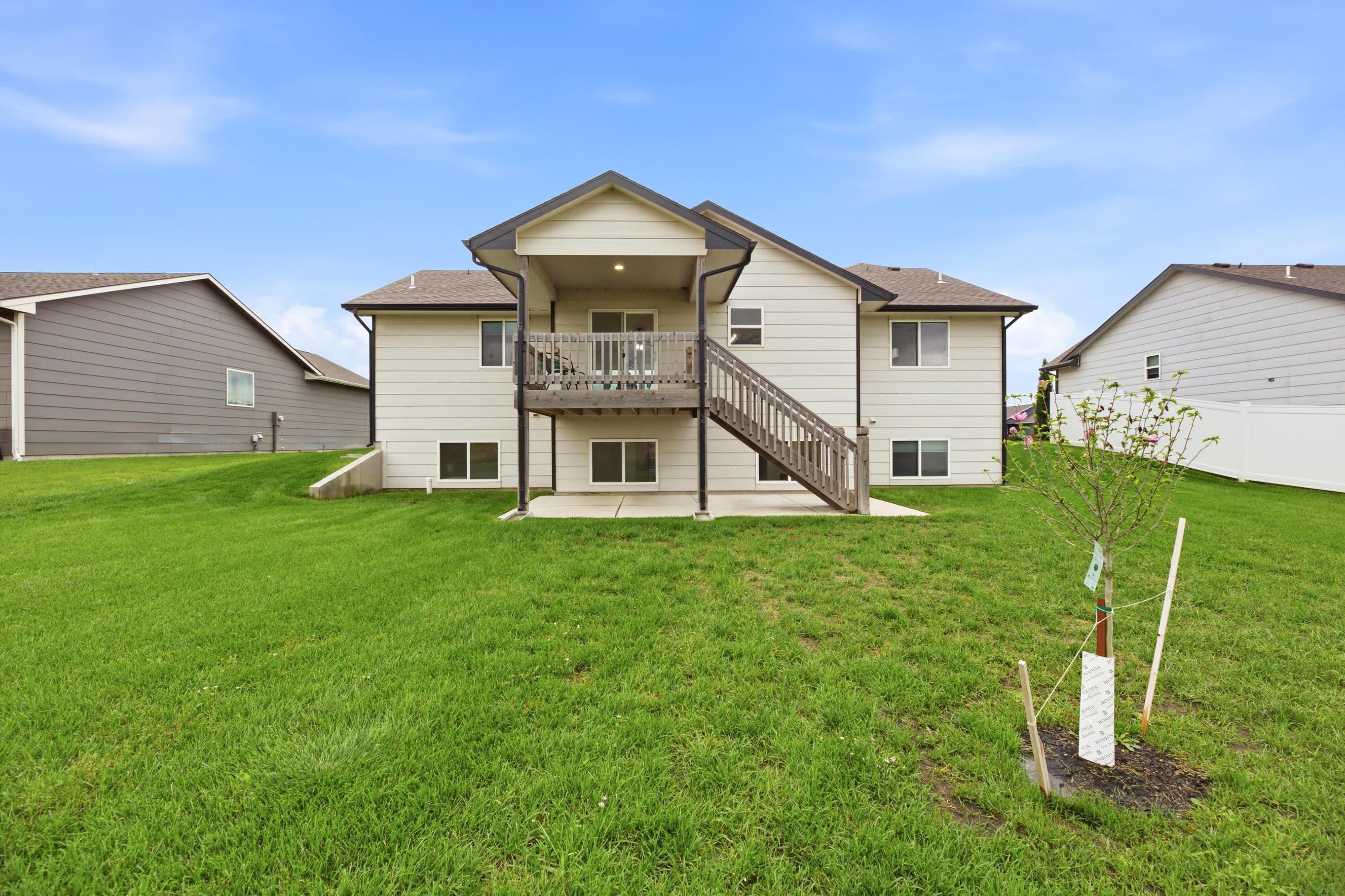 Rear of a two-story house with a covered deck, wooden stairs, and a broad grassy backyard.