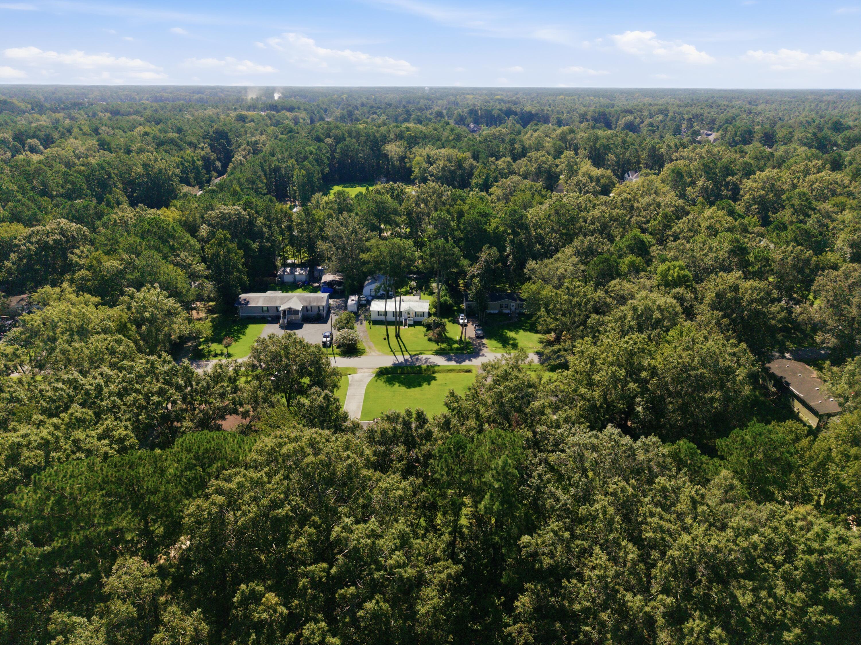 Aerial view of a home and neighboring houses amid dense woods, with a large lawn and driveway.