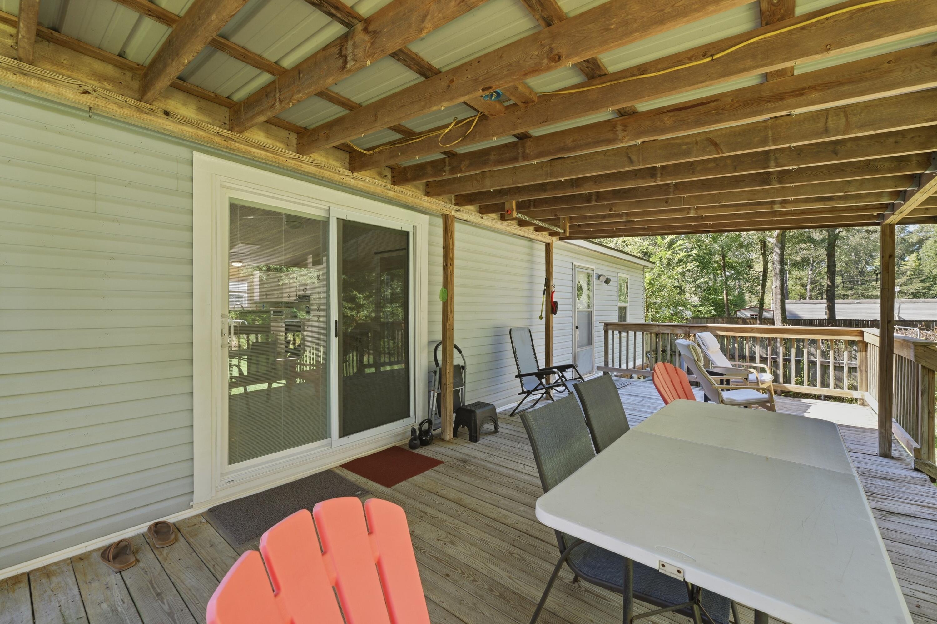 Covered wooden deck with exposed beams, sliding glass doors, and outdoor dining furniture.