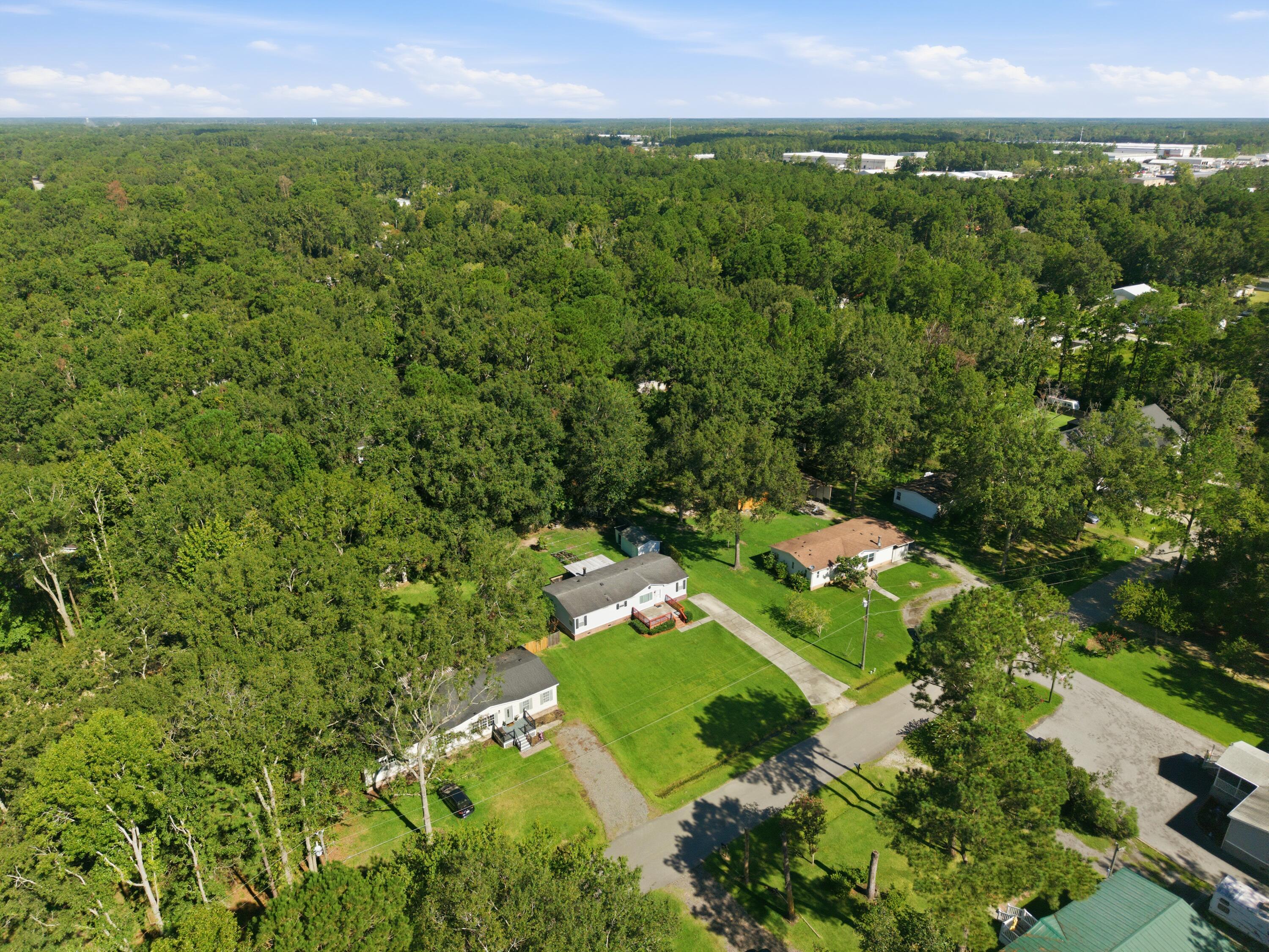 Aerial view of a white home and lawn surrounded by dense woods and neighboring houses.