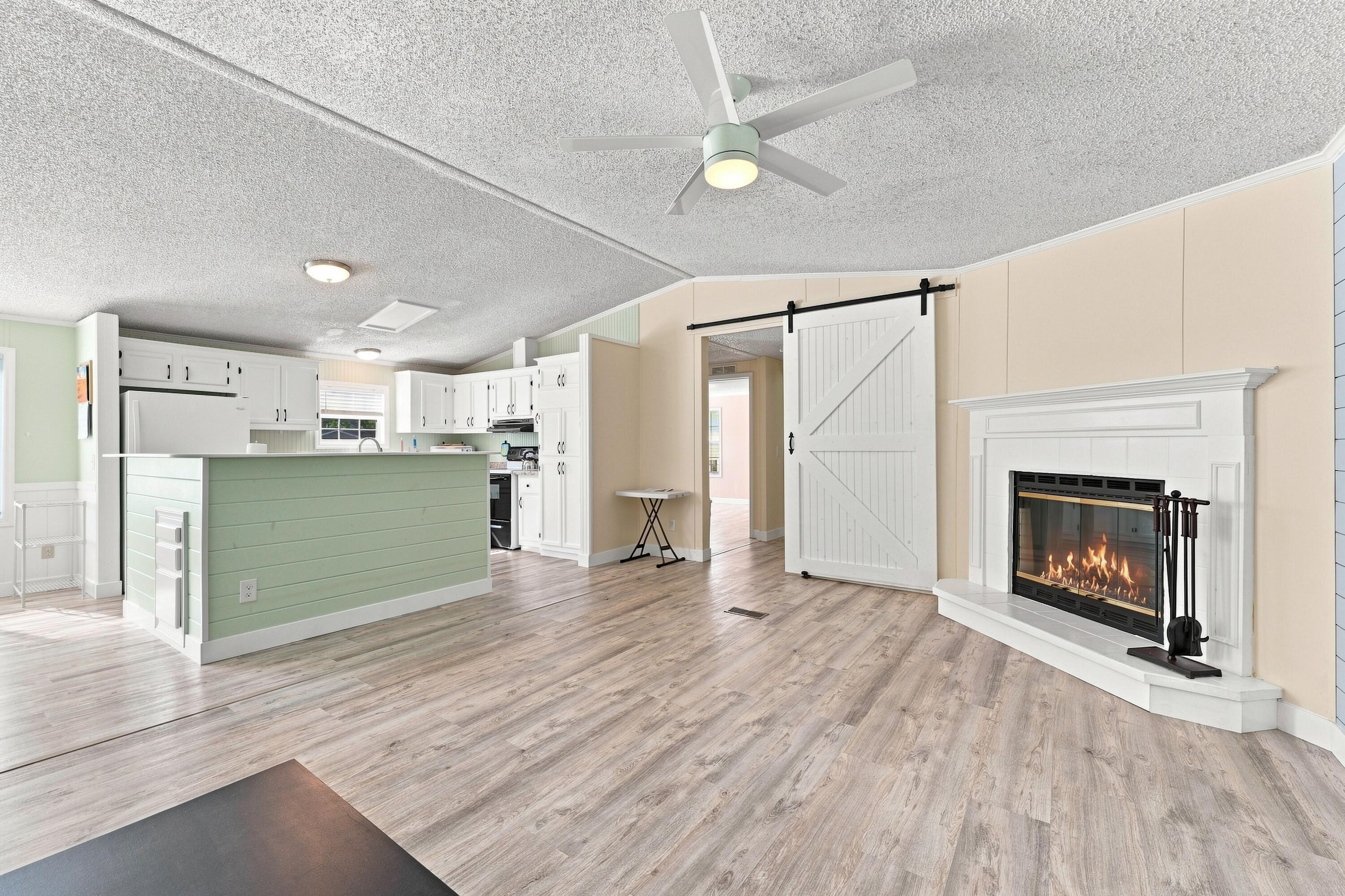 Open-plan living room and kitchen with a white fireplace, pale green island, and sliding barn door.