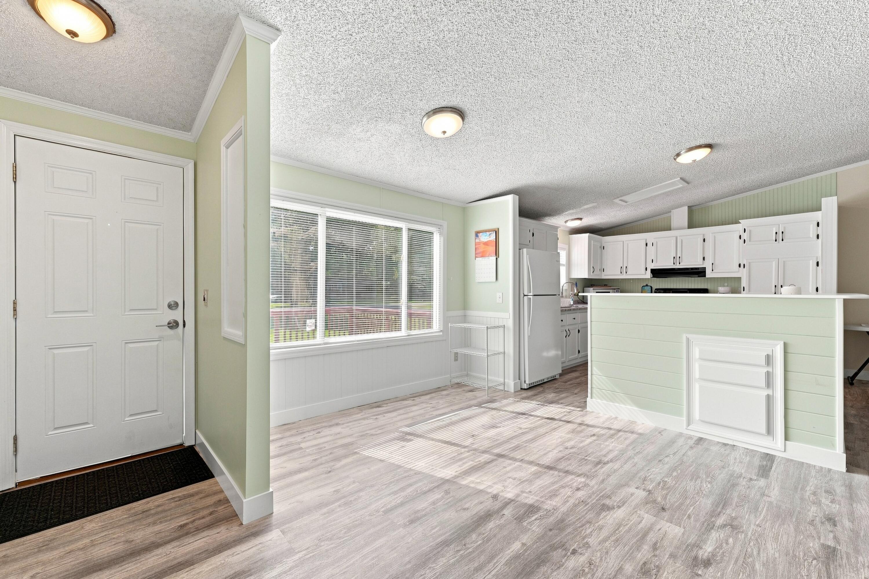 Entry opens to a bright kitchen with white cabinets, pale green island, and gray wood-look floors.