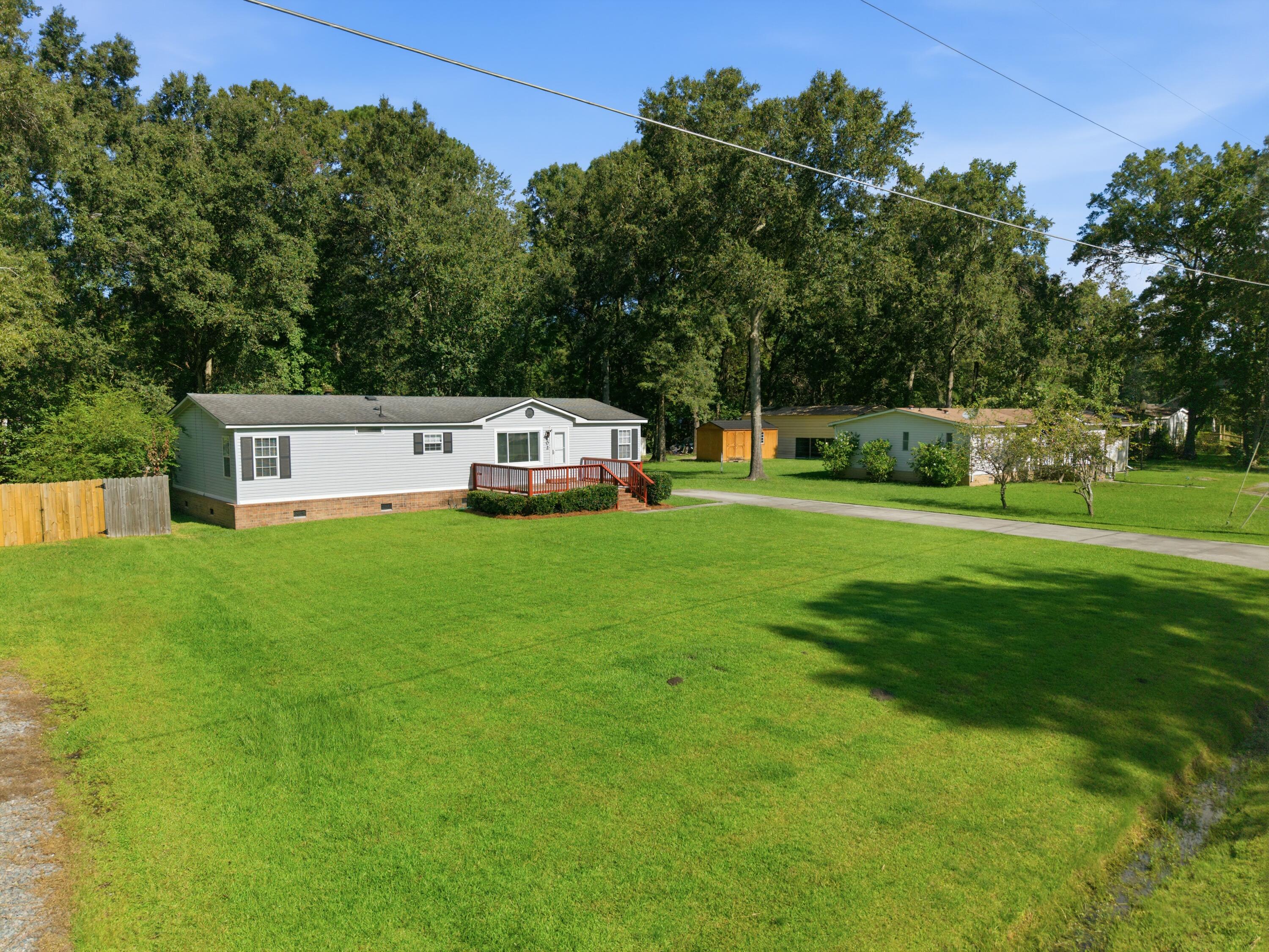 Light-colored home with a red front deck and broad lawn, backed by mature trees.