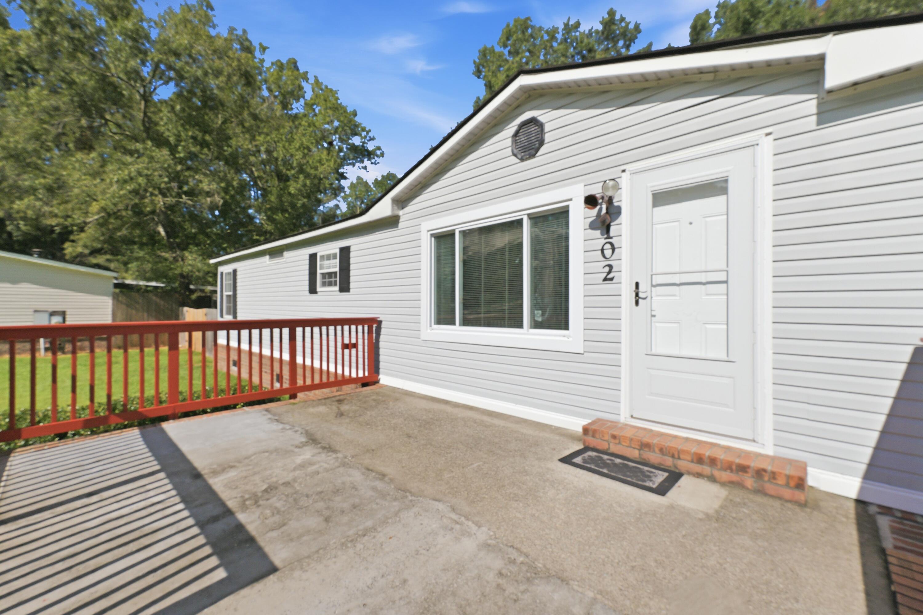 Home entrance with white siding, a brick step, and a concrete patio bordered by red railing.