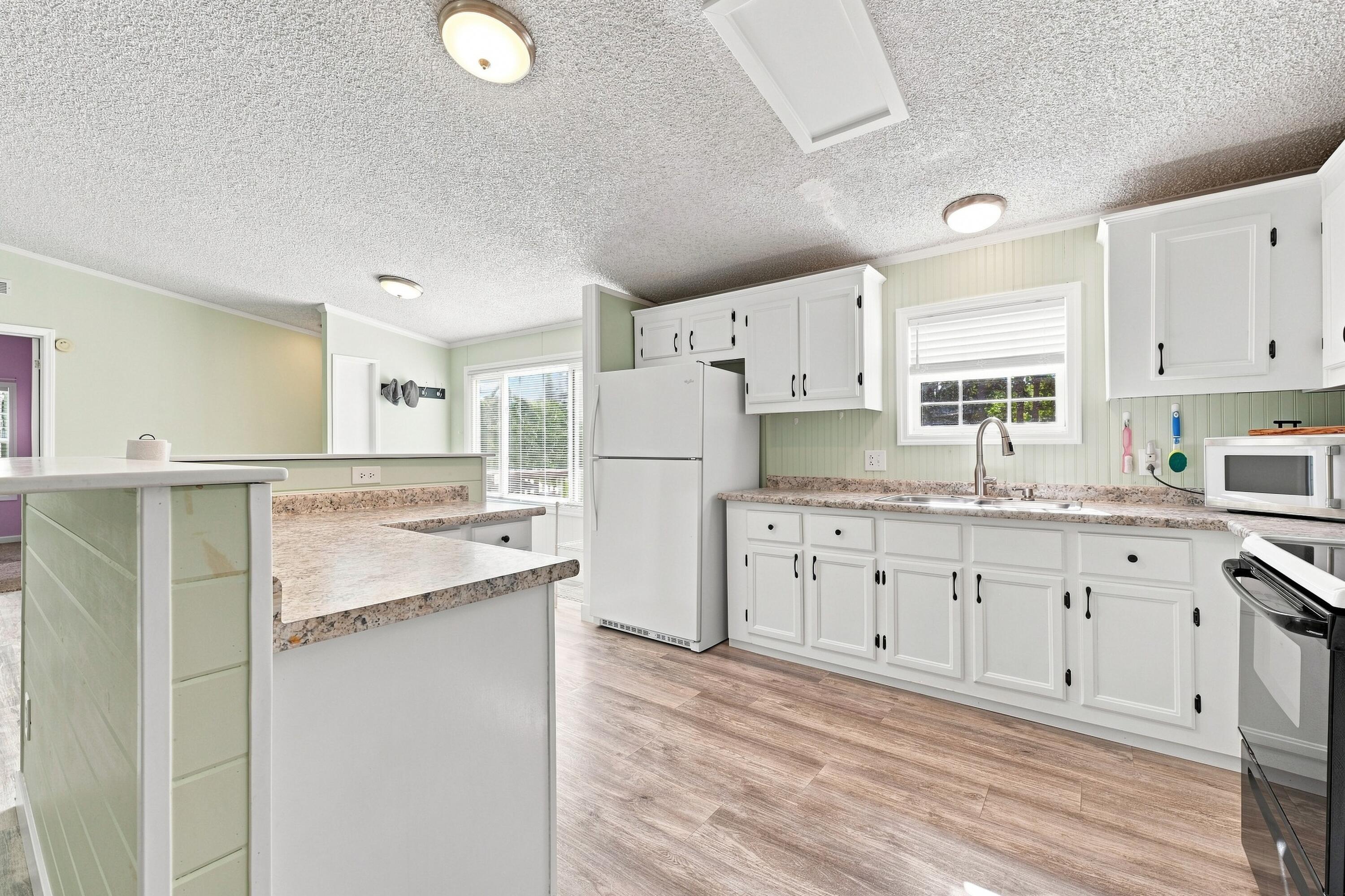 Kitchen with white cabinets, pale green walls, and a large speckled-countertop peninsula.