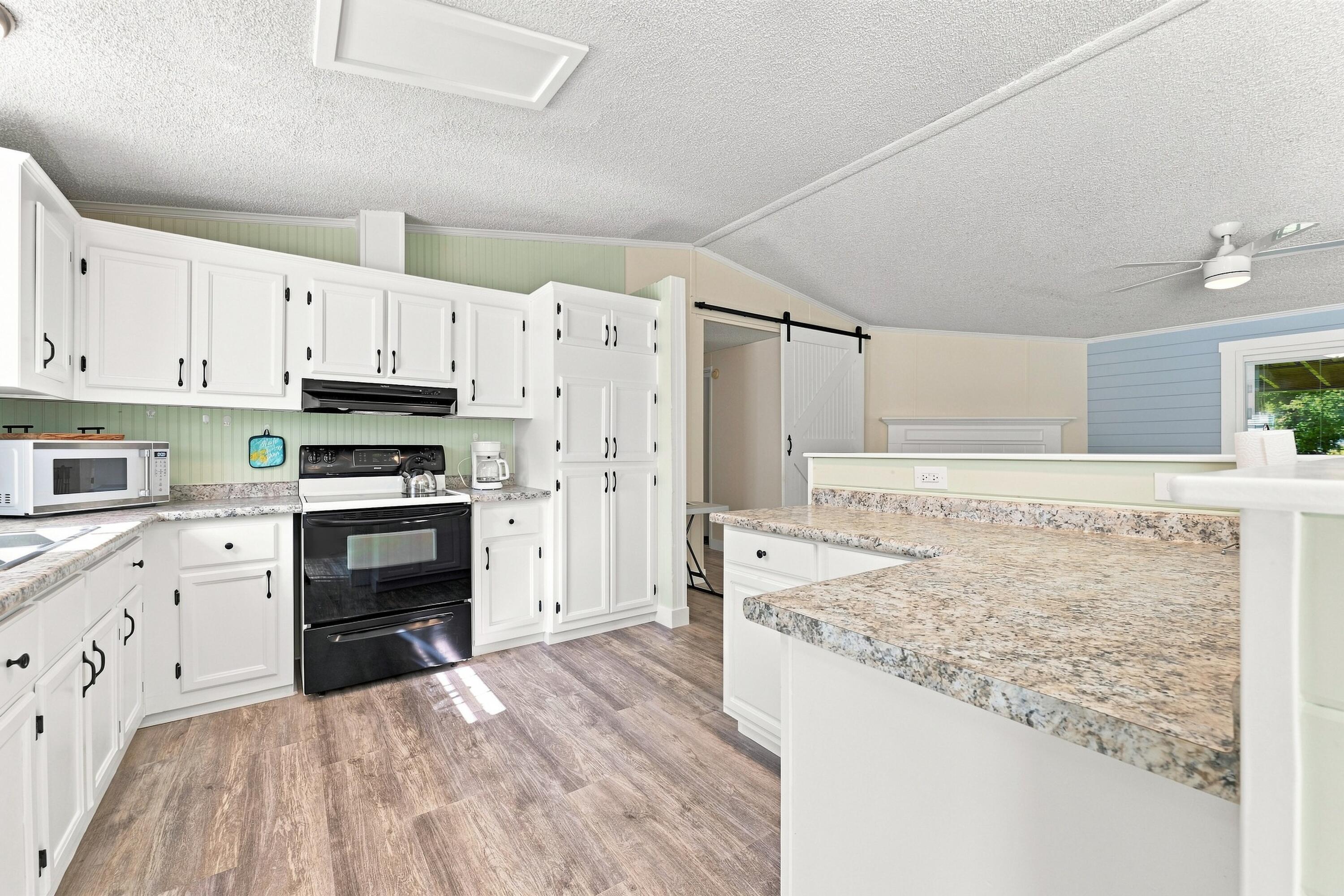 Kitchen with white cabinetry, a black range, and a large speckled-stone peninsula.