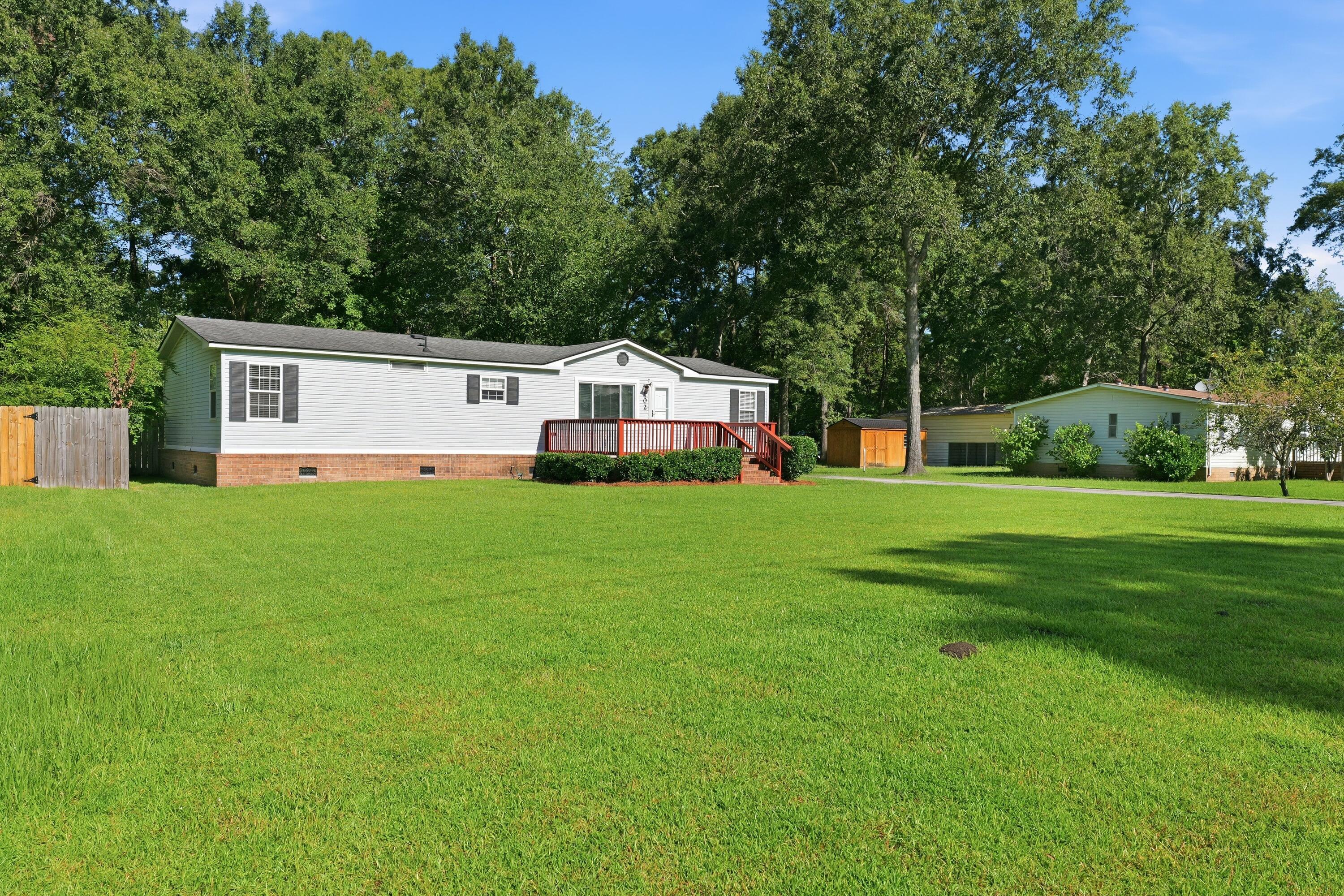 White single-story home with a brick foundation and red-railed porch behind a broad lawn.