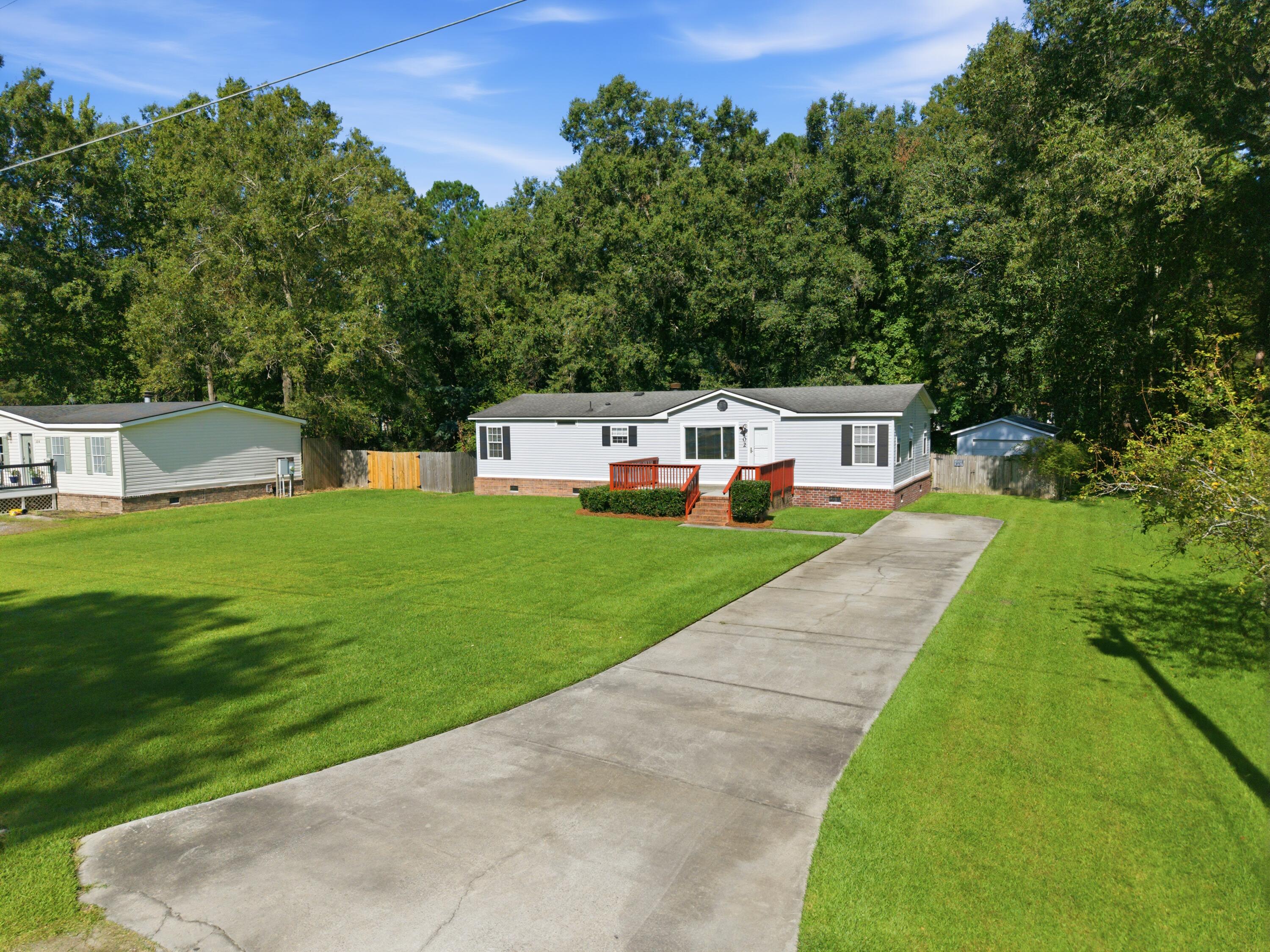 White single-story home with a red-railed entry deck, broad lawn, and long concrete driveway.
