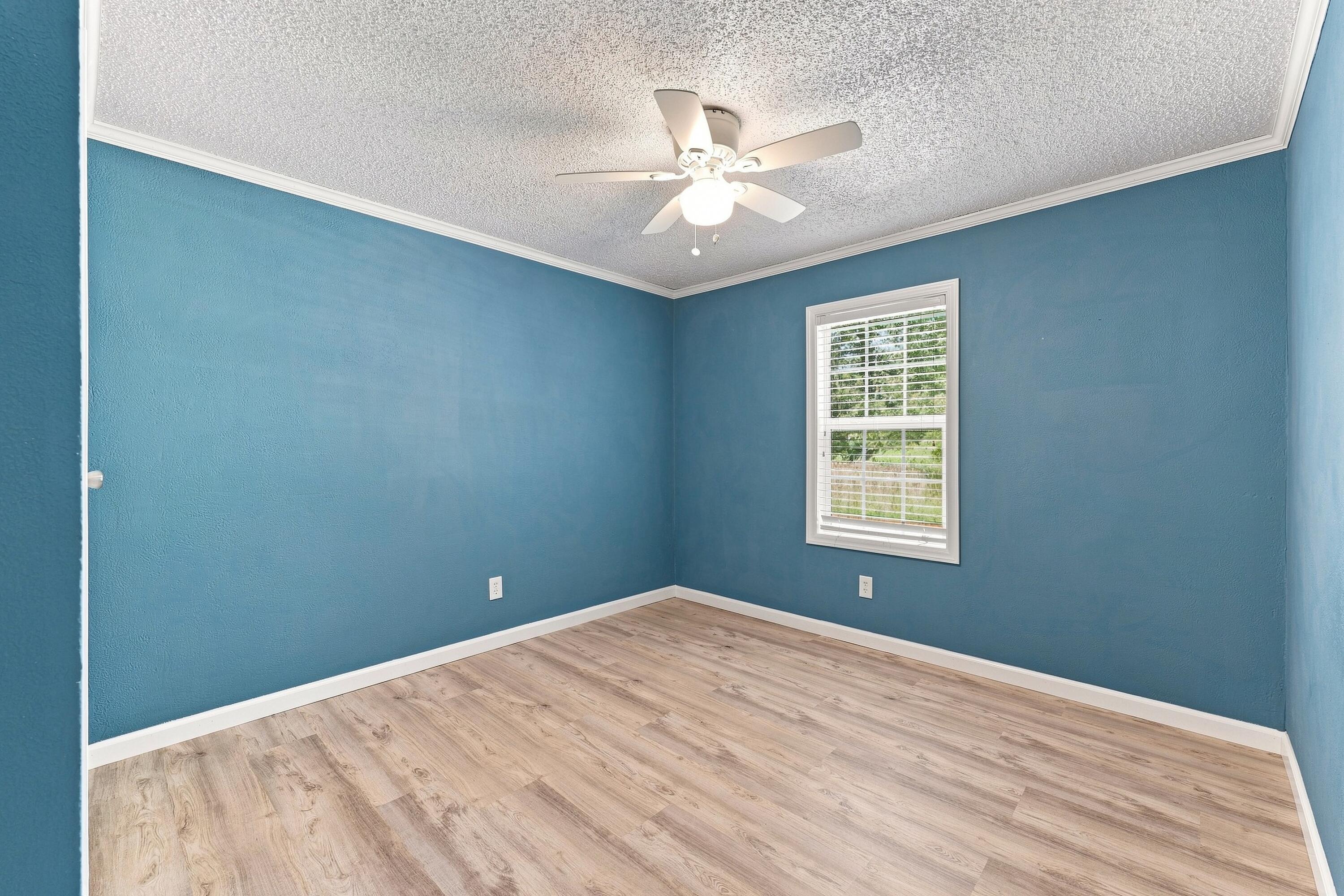 Empty blue room with light wood-look flooring, a window with blinds, and a ceiling fan.