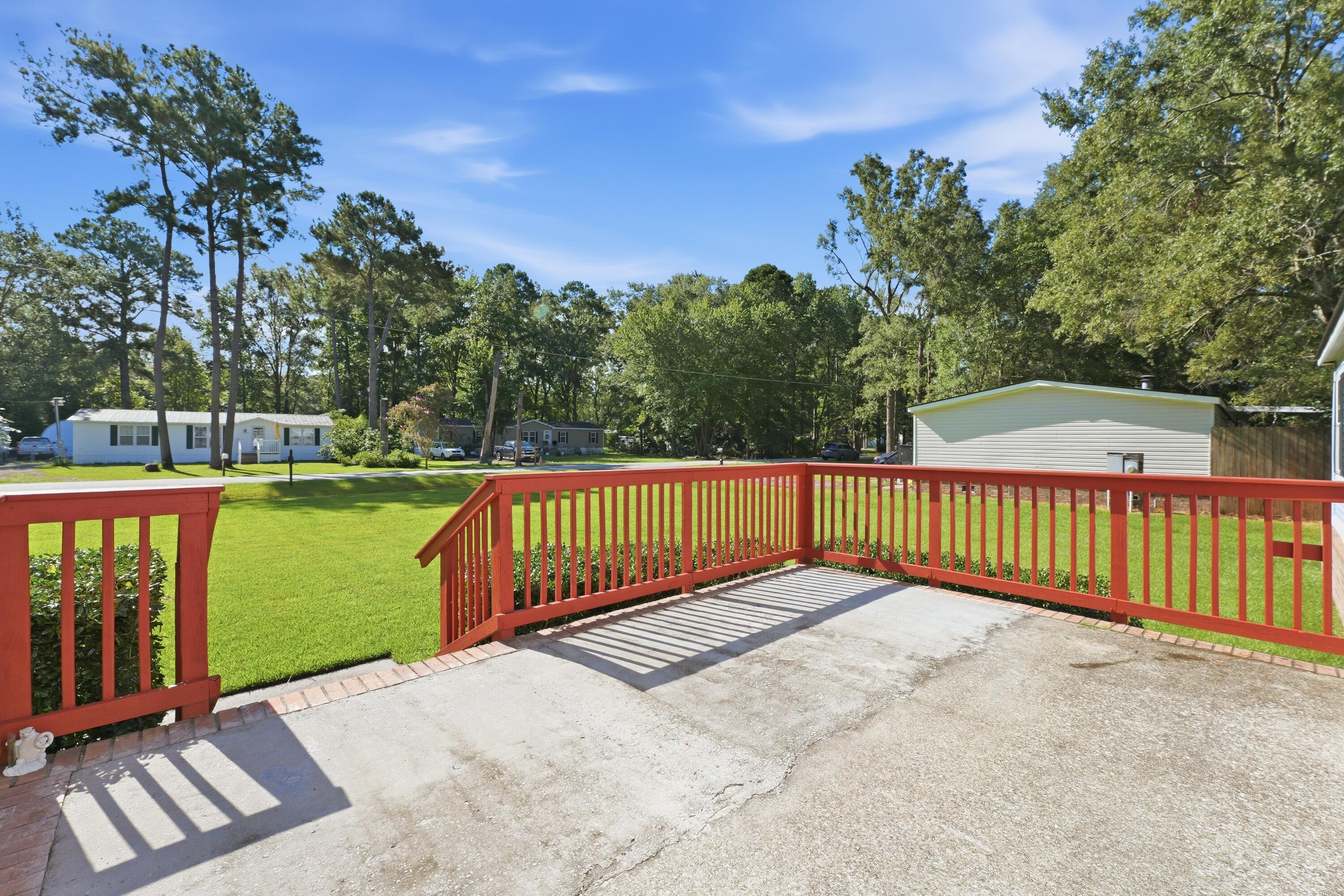 Concrete patio with red railings overlooking a green lawn and mature trees.
