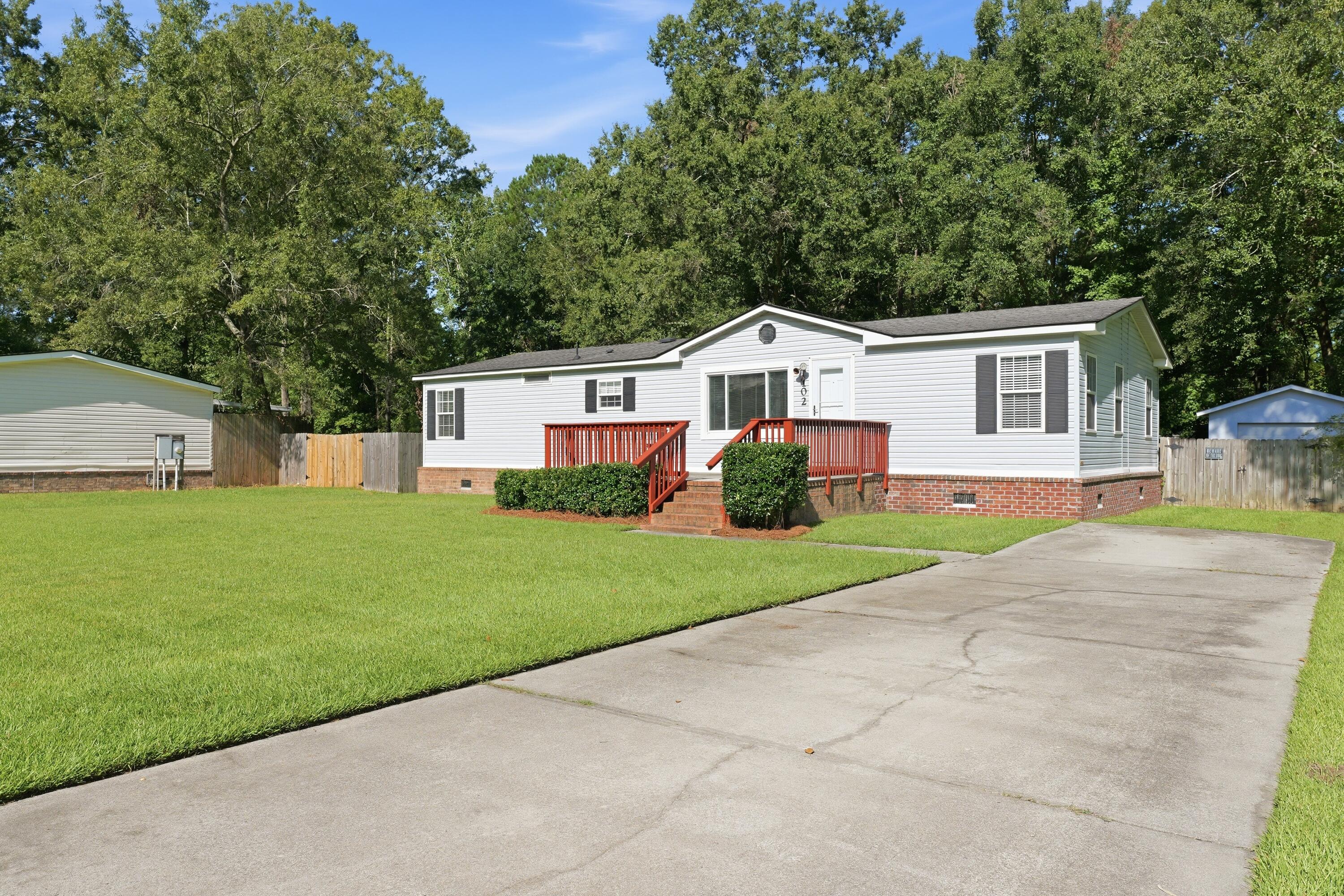 White single-story home with red porch railings, brick foundation, and a broad concrete driveway.