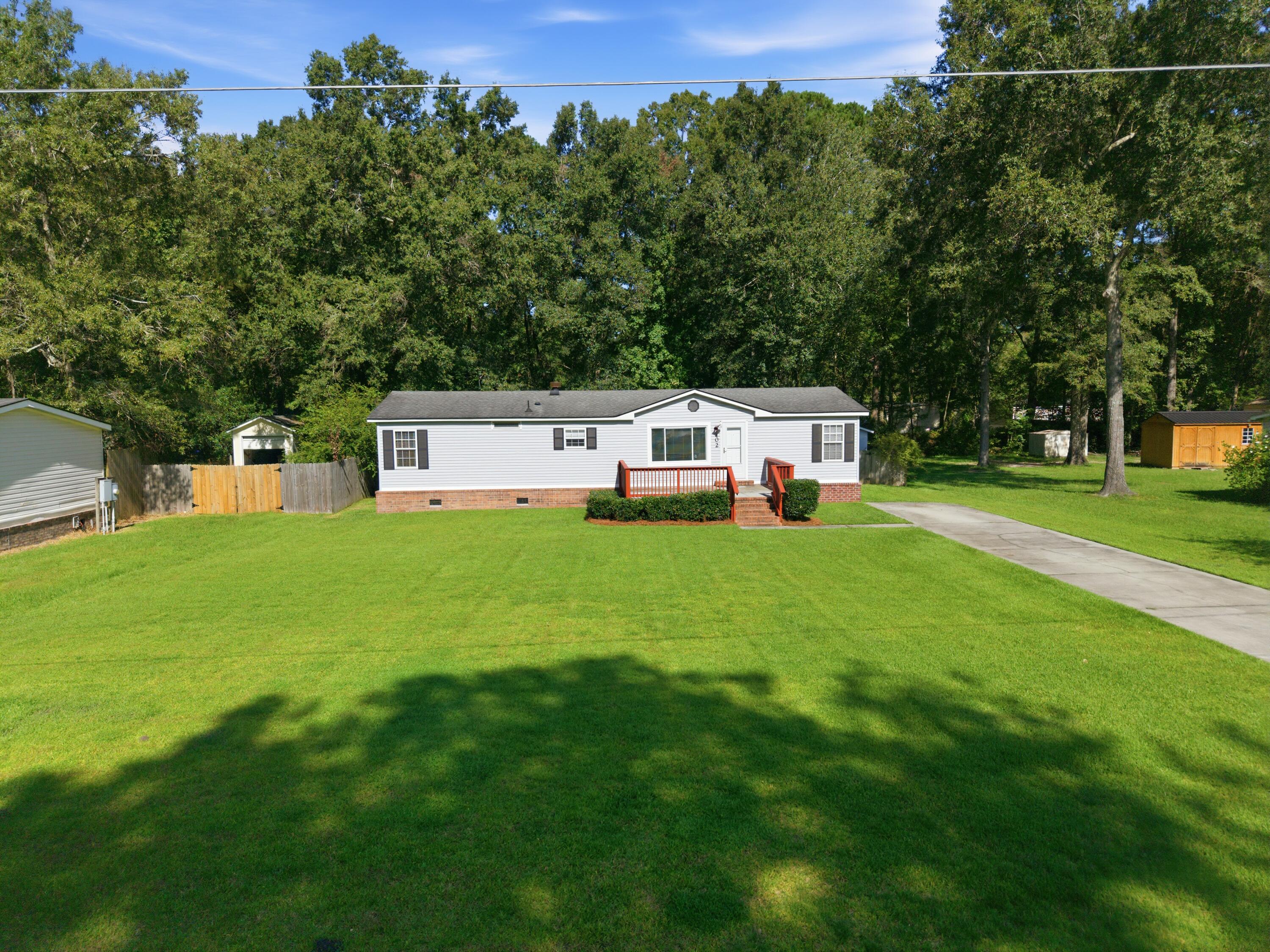 White single-story home with red entry steps, a wide lawn, and mature trees behind it.