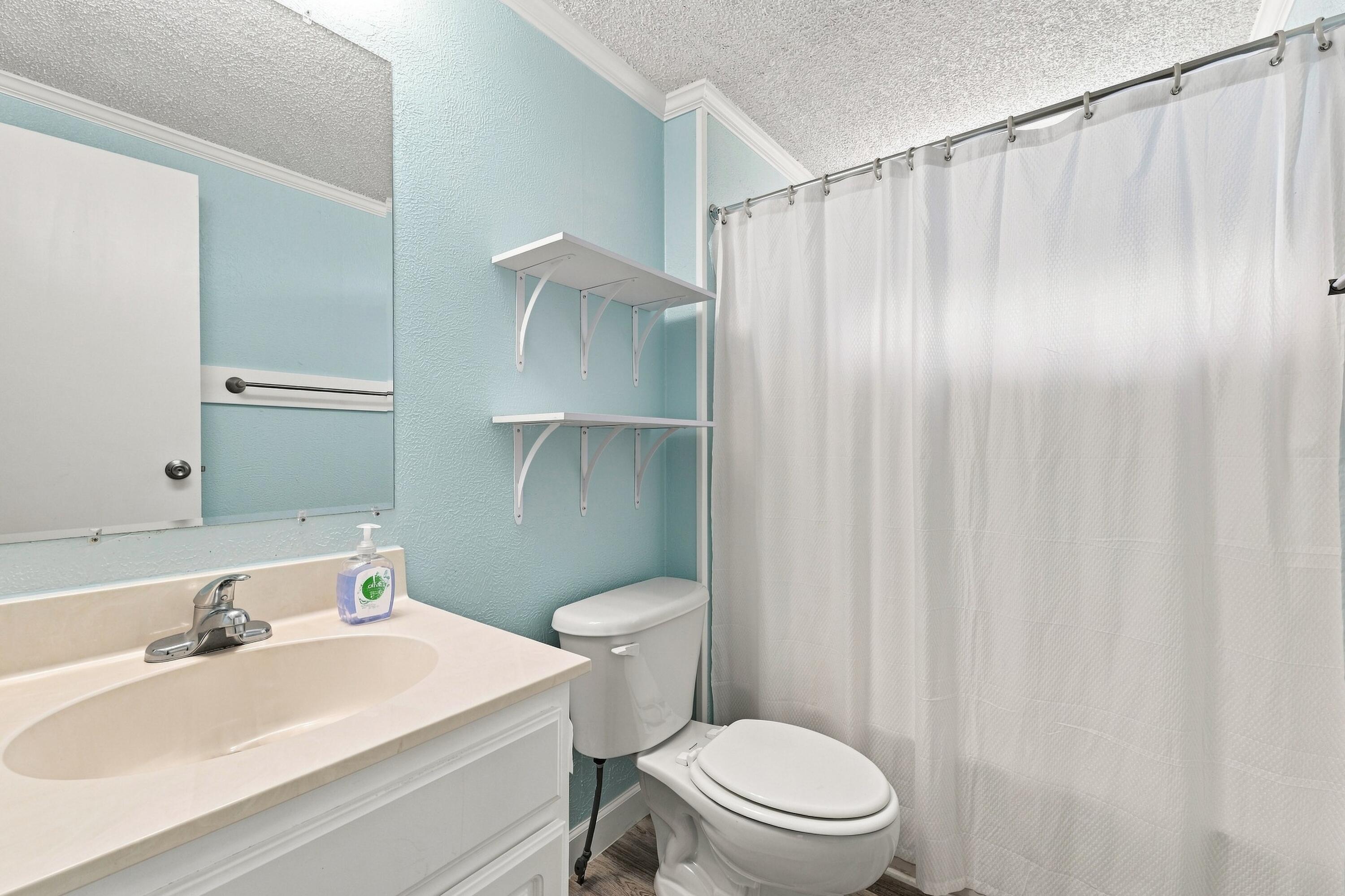 Bathroom with light blue walls, white vanity, wall shelves, and a white shower curtain.