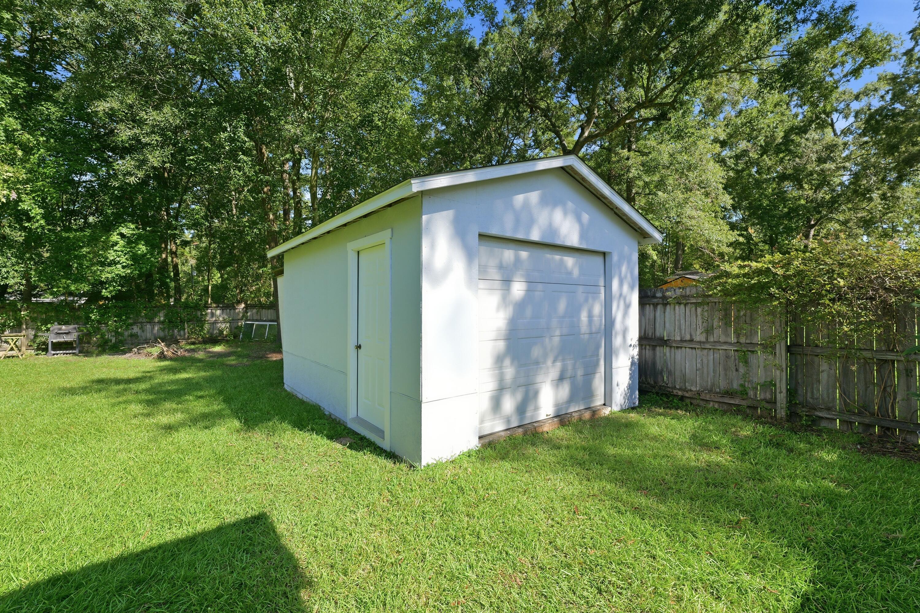 White detached garage with overhead and side-entry doors in a fenced, tree-shaded backyard.