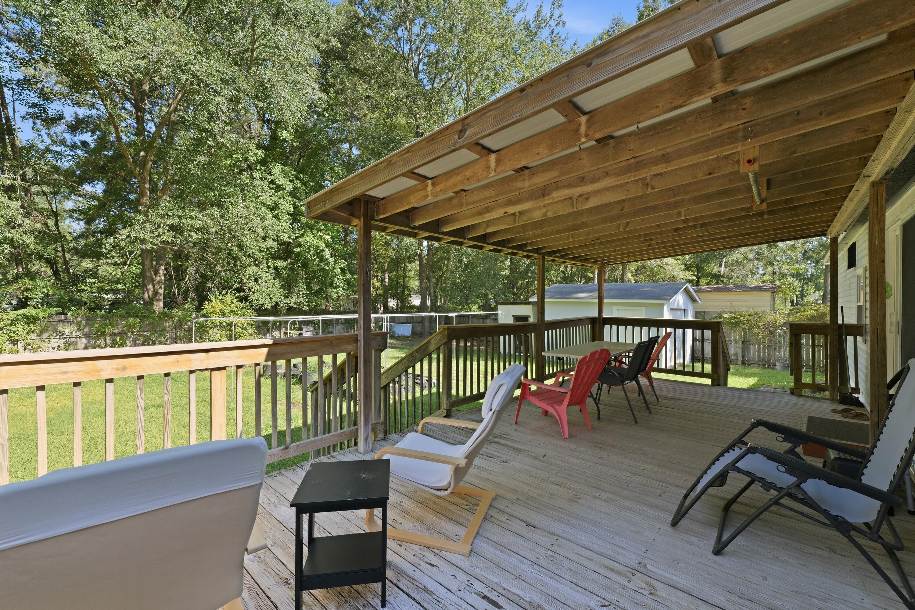Covered wooden deck with lounge chairs overlooks a grassy, tree-lined backyard.